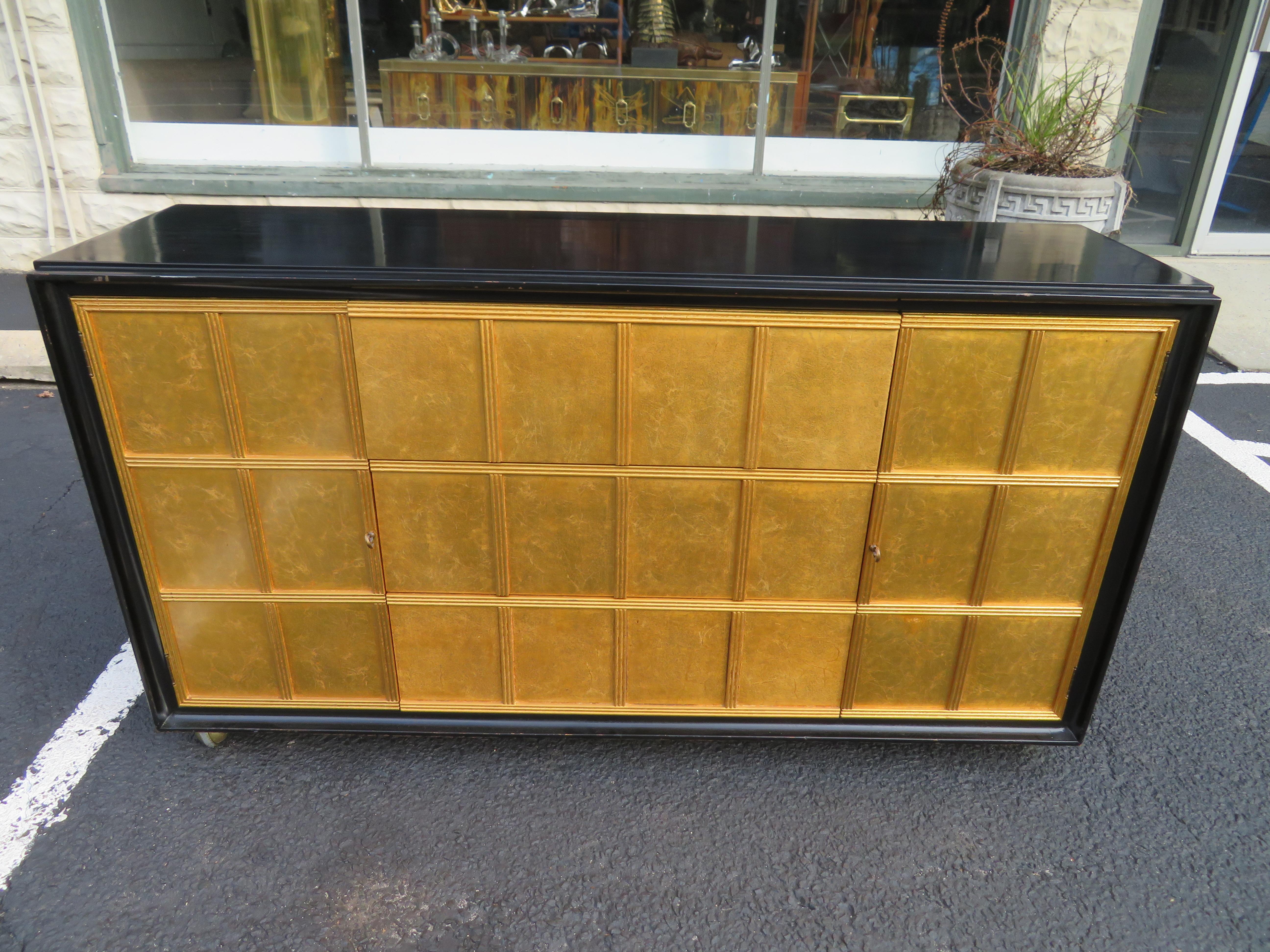Lovely Dorothy Draper style gold leaf front rolling buffet credenza. We love the gold leafed front lattice style doors and drawers. There are drawers down the middle with two doors on either side-one adjustable shelf in each. The top and sides