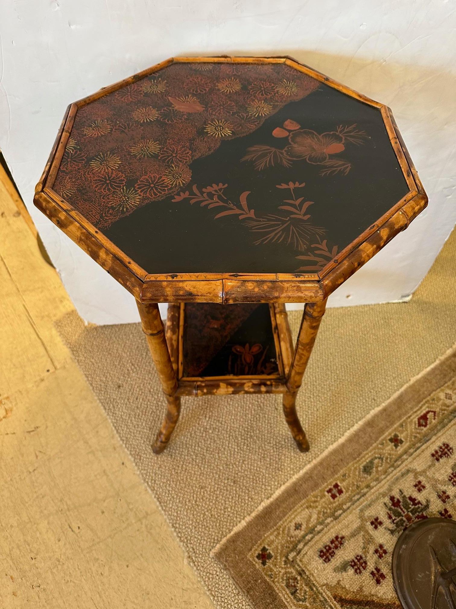 Pretty vintage bamboo octagonal side table having black lacquer top and second square tier with red and gold floral decoration.
