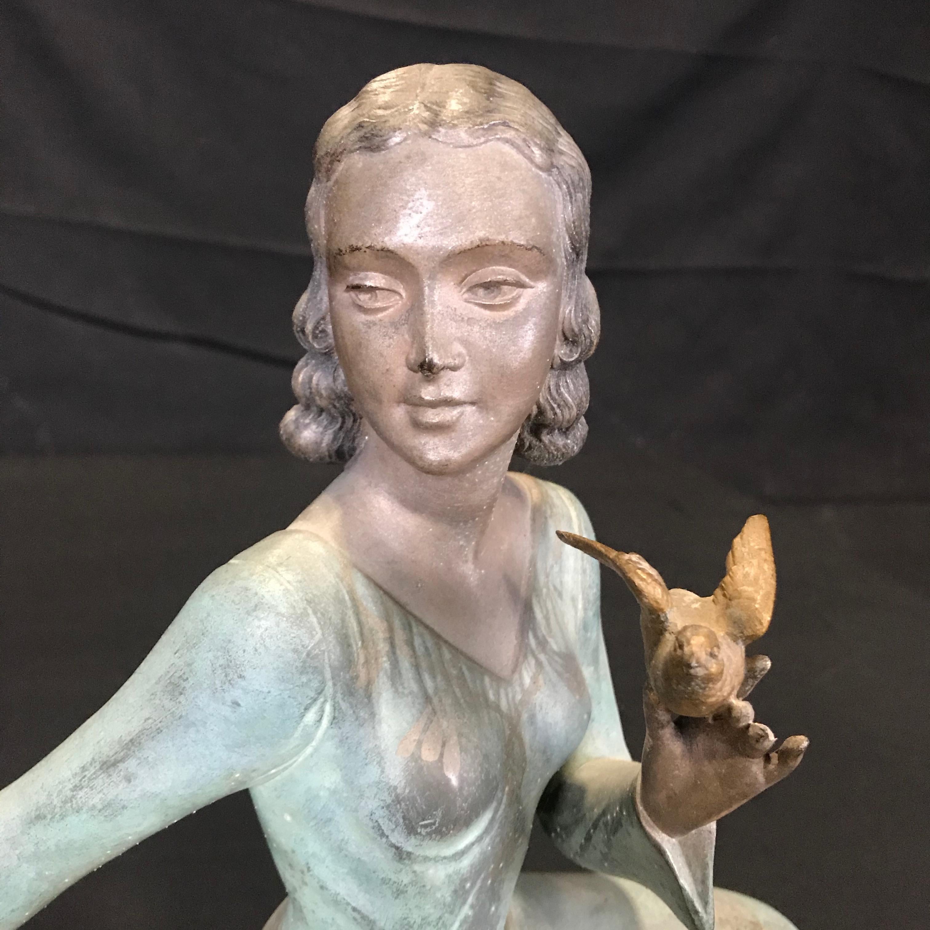 Stunning French Art Deco bronze patina spelter figure gracefully kneeling and decorated in two colors: bronze patinated blue color for her dress and gilt color for her birds and waist belt. The base is beautiful Portoro marble, signed by the