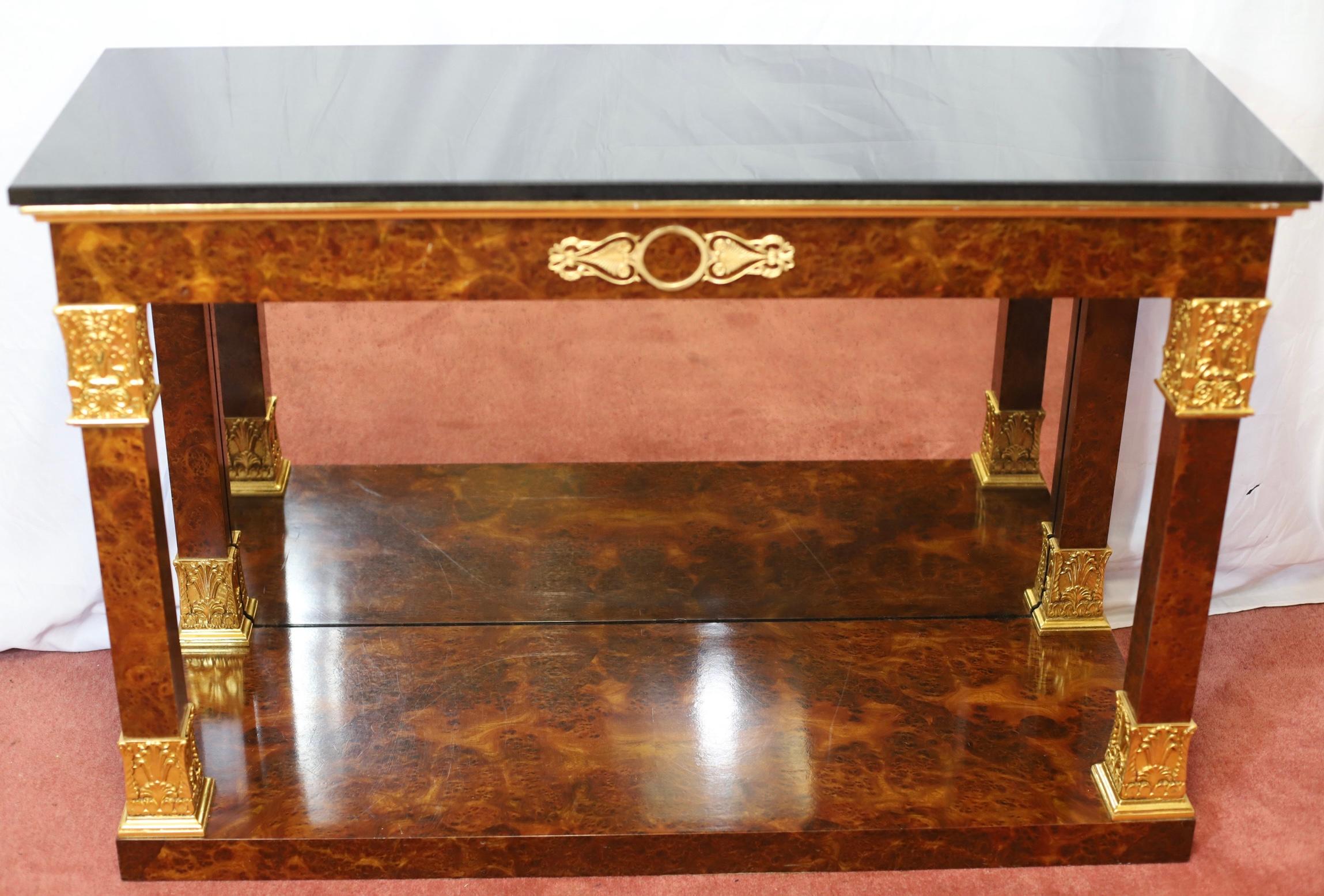 Nos complace poner a la venta esta impresionante consola de estilo imperio francés del SIGLO XX, con tablero de chapa de madera pulida y piedra negra, superficie rectangular elevada sobre cuatro patas cónicas cuadradas decoradas con monturas de