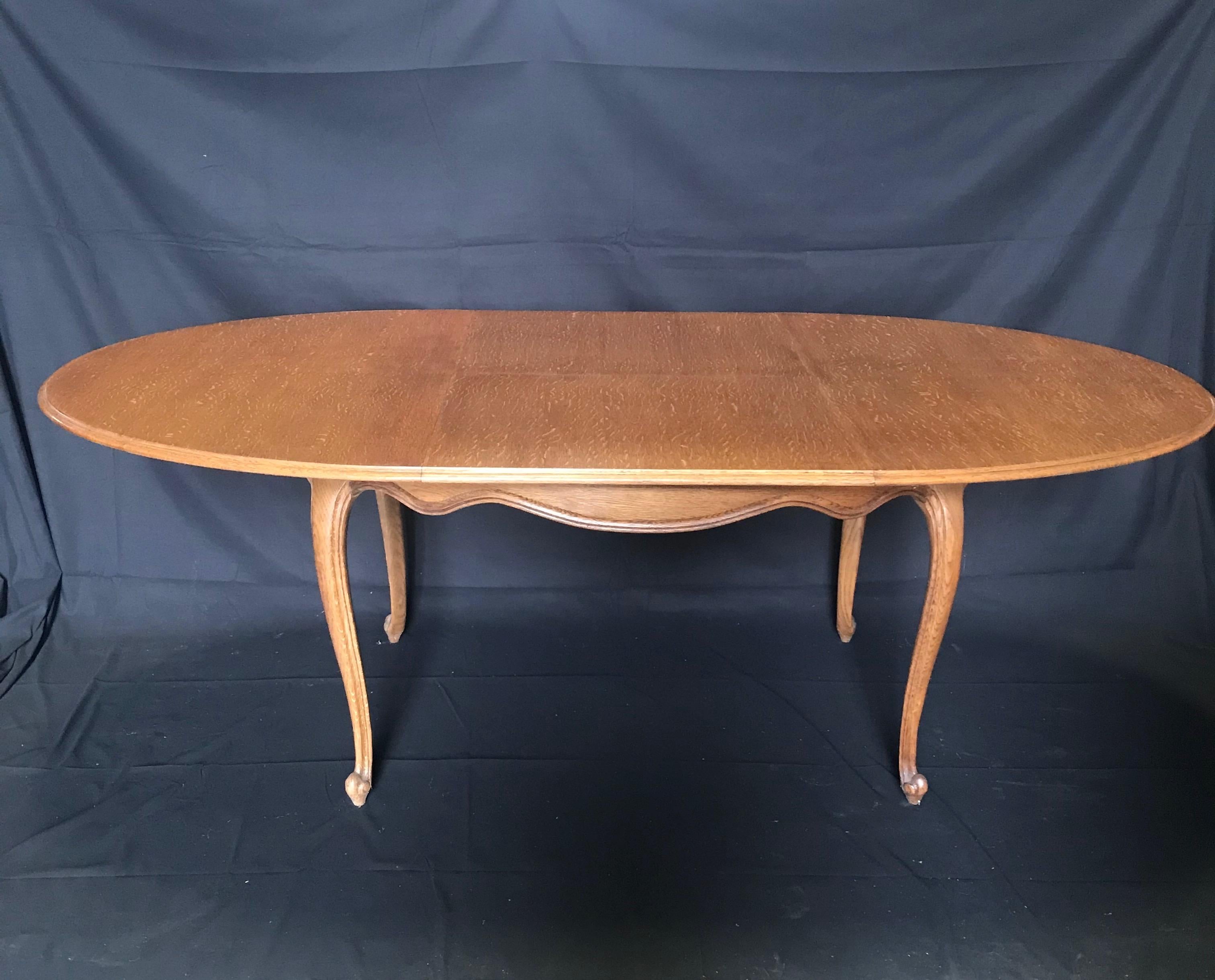 A lovely Louis XV style oak dining table with carved undulating apron and cabriole legs that has an intricate, very French inset extension mechanism that will allow the table to close to a length of 5 feet, or open up to 7 ft. 3 inches. The carvings