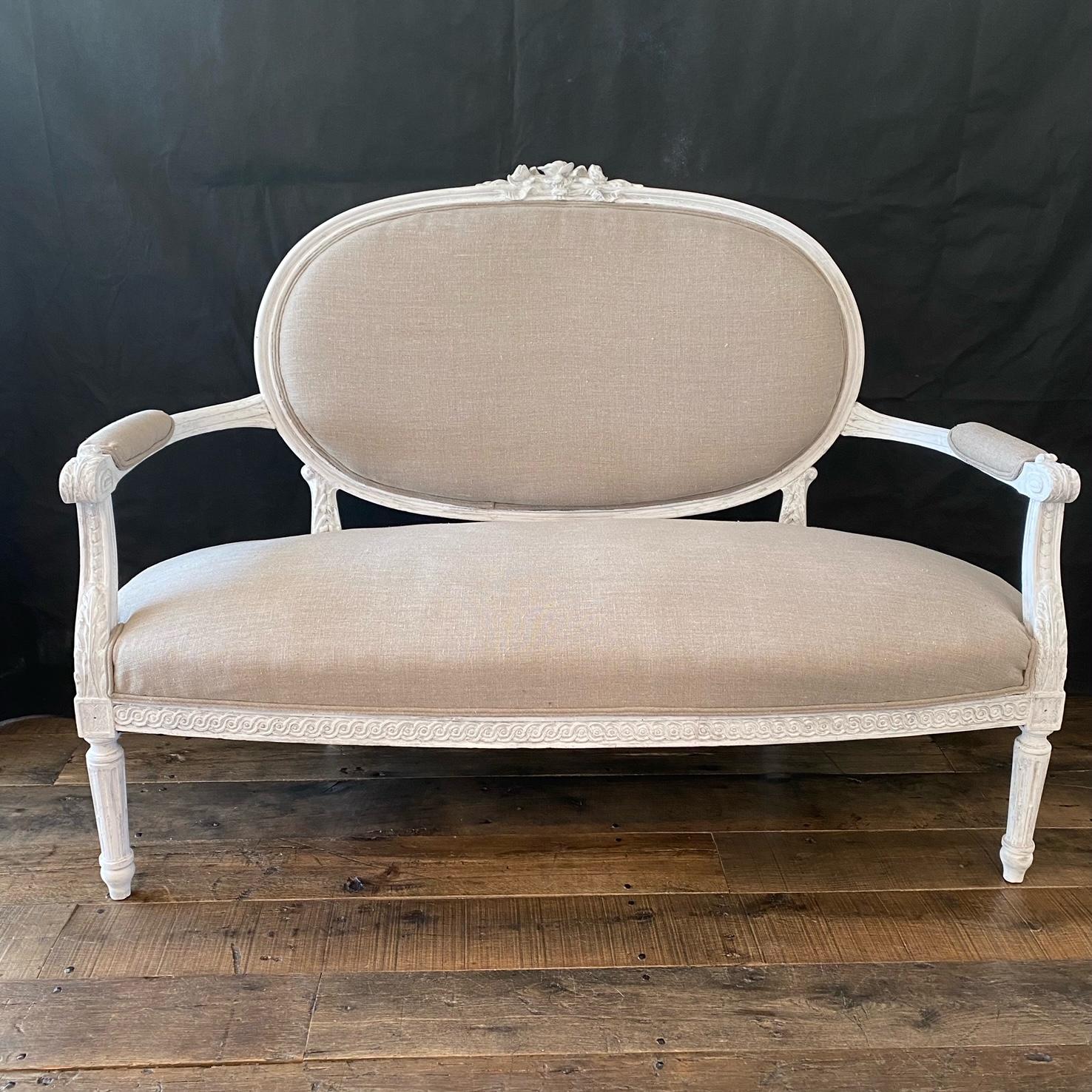 A very pretty late 19th century three piece Louis XVI style parlor set consisting of a settee and a pair of arm chairs having beautiful carved designs on the painted arms and legs and classic oval backs. Newly reupholstered in a French linen cotton