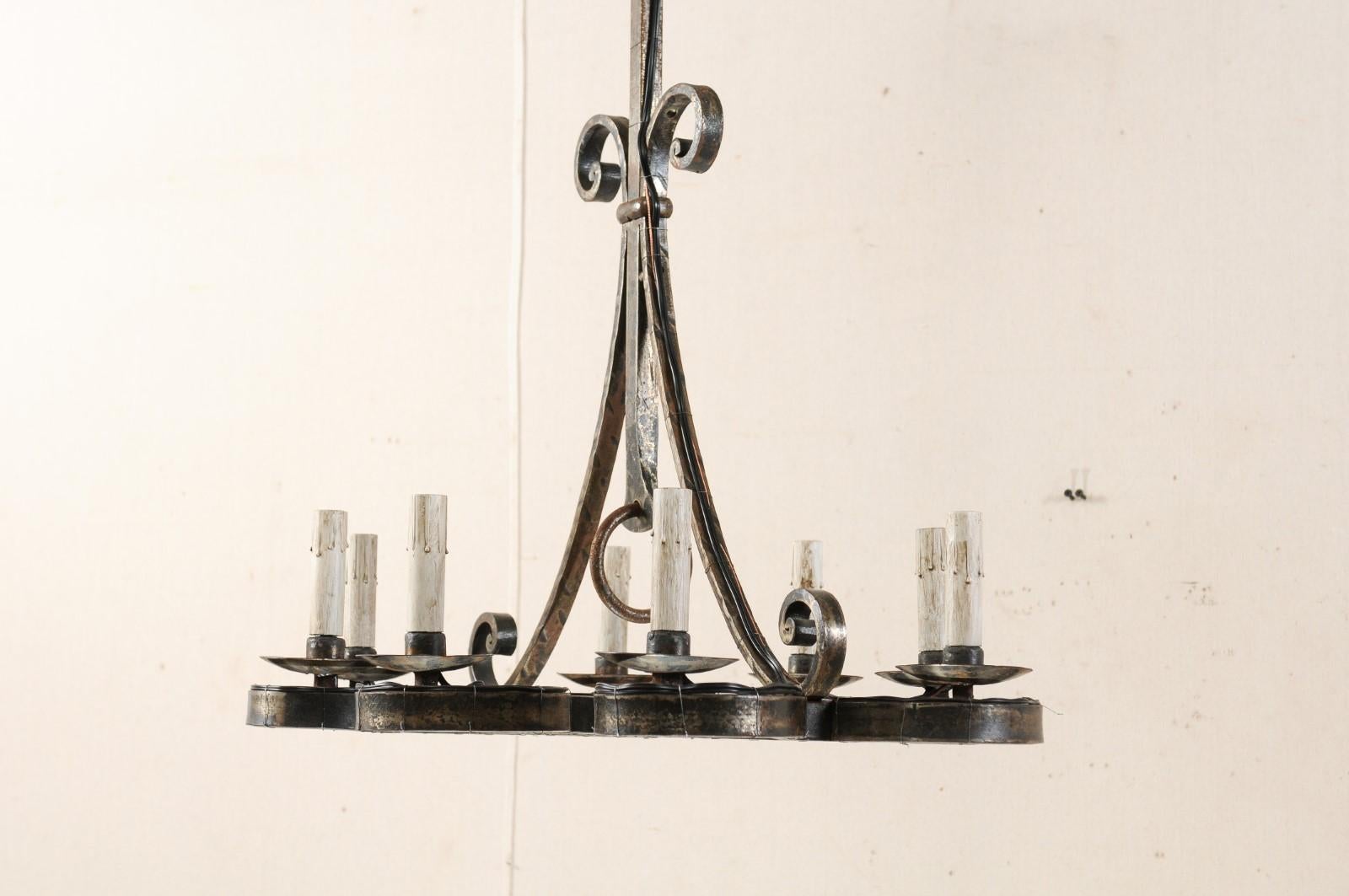 A French mid-20th century suspended eight-light forged-iron chandelier. This vintage French chandelier features a central gallery made up of downward facing scrolled iron bands, whereas each perimeter scroll is topped with an iron bobèche and
