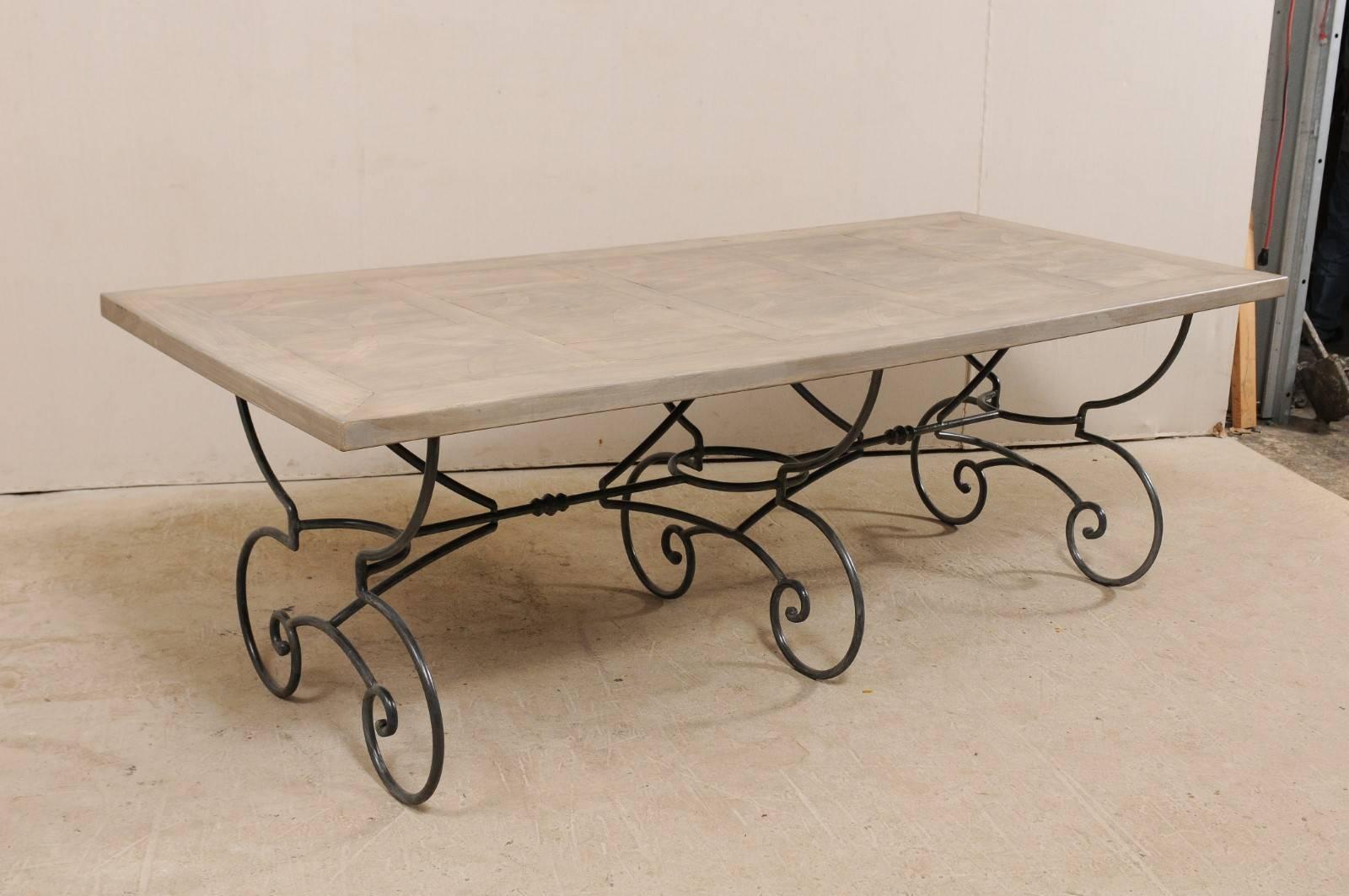 A French mid-20th century wood top table with scrolling iron base. This French vintage table features an inlay wood top, decorated with geometrical patterns framed within its centre, resting upon an ornate iron base. The base of the table is