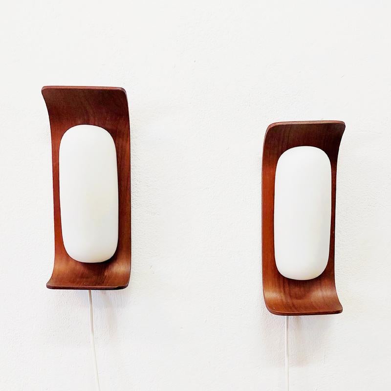 Lovely Italian pair of teak and opaline glass wall lamps designed by designer Goffredo Reggiani for Reggiani Illuminazione in the 1960s.
The lamps has a nicely curved teak back plate with a rectangular shape holding a white oval shaped opaline glass