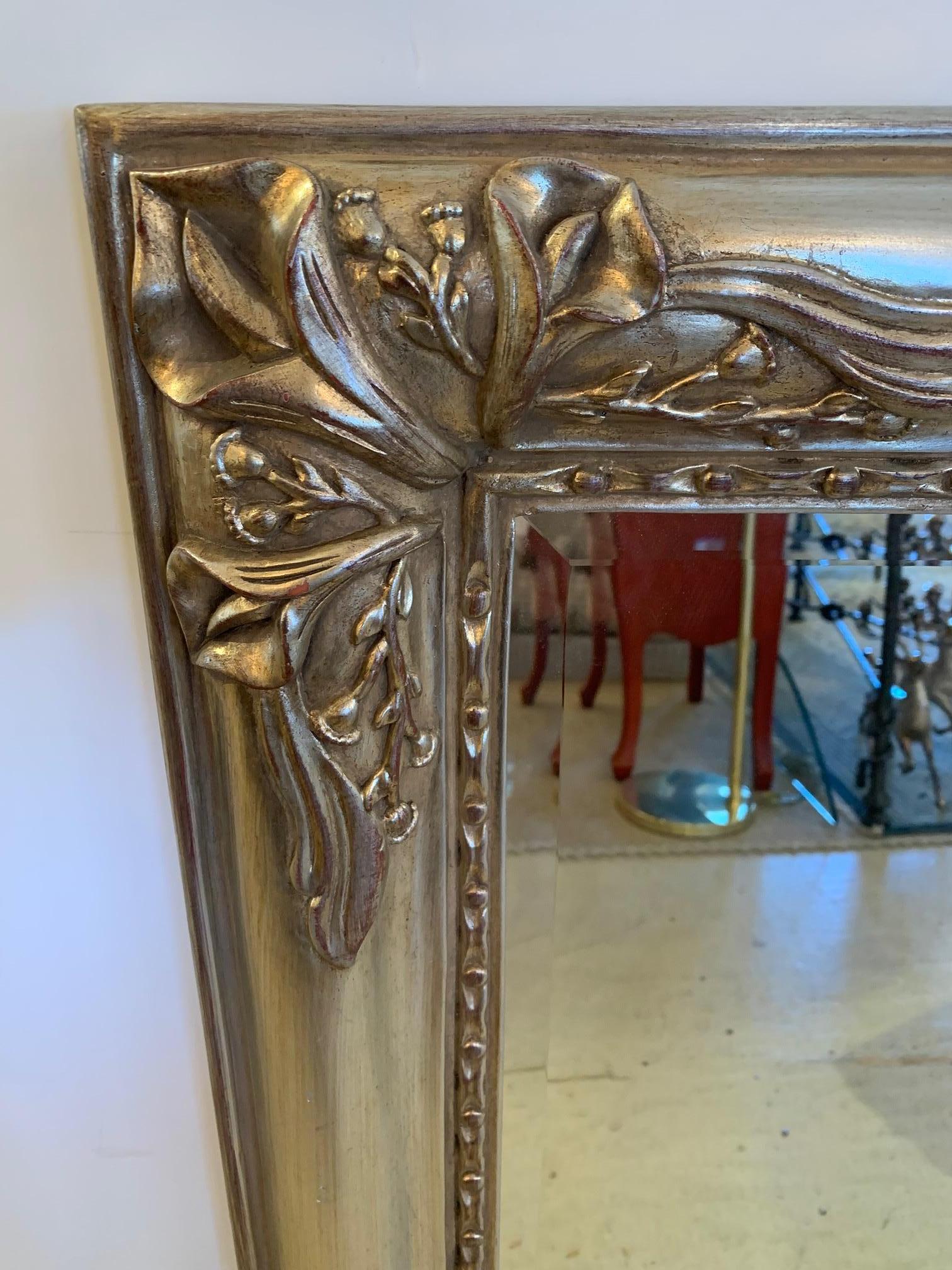 Beautiful bevelled rectangular mirror having silver giltwood carved frame adorned with calla lilies.