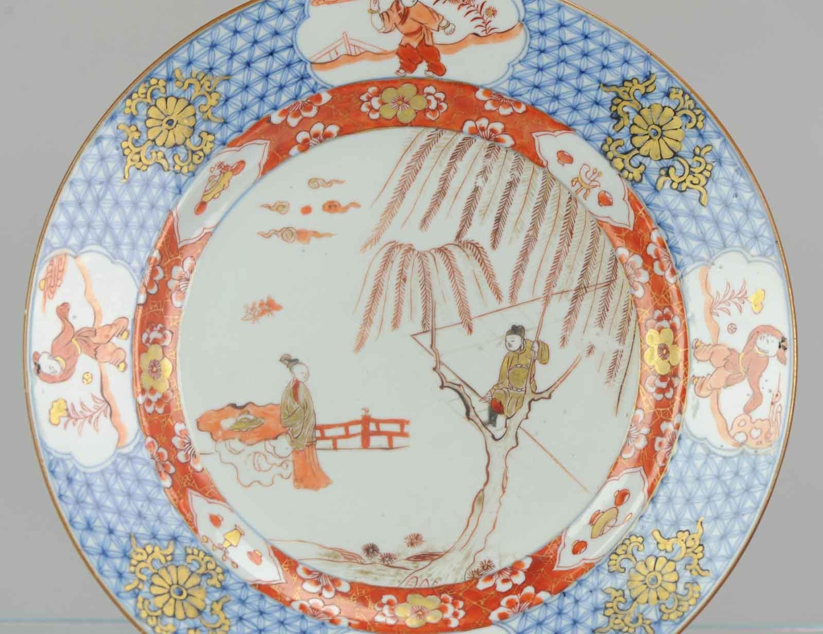 Dish on footring with a flat, underglaze brown-edged, rim (jia mangkou). Chinese Imari, decorated in underglaze blue, overglaze iron-red, black and gold. Very interesting scene of a figure trying to reach something in the tree. A women is looking at