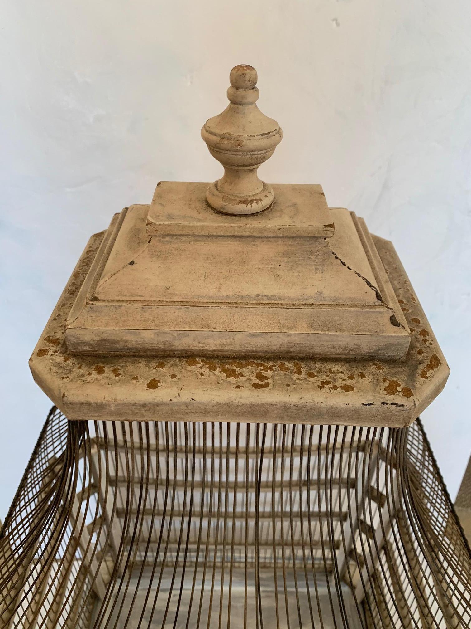 A large functional country style vintage birdcage having weathered grey painted natural wood and wire construction, door that opens, and new bottom tray that pulls out for cleaning.