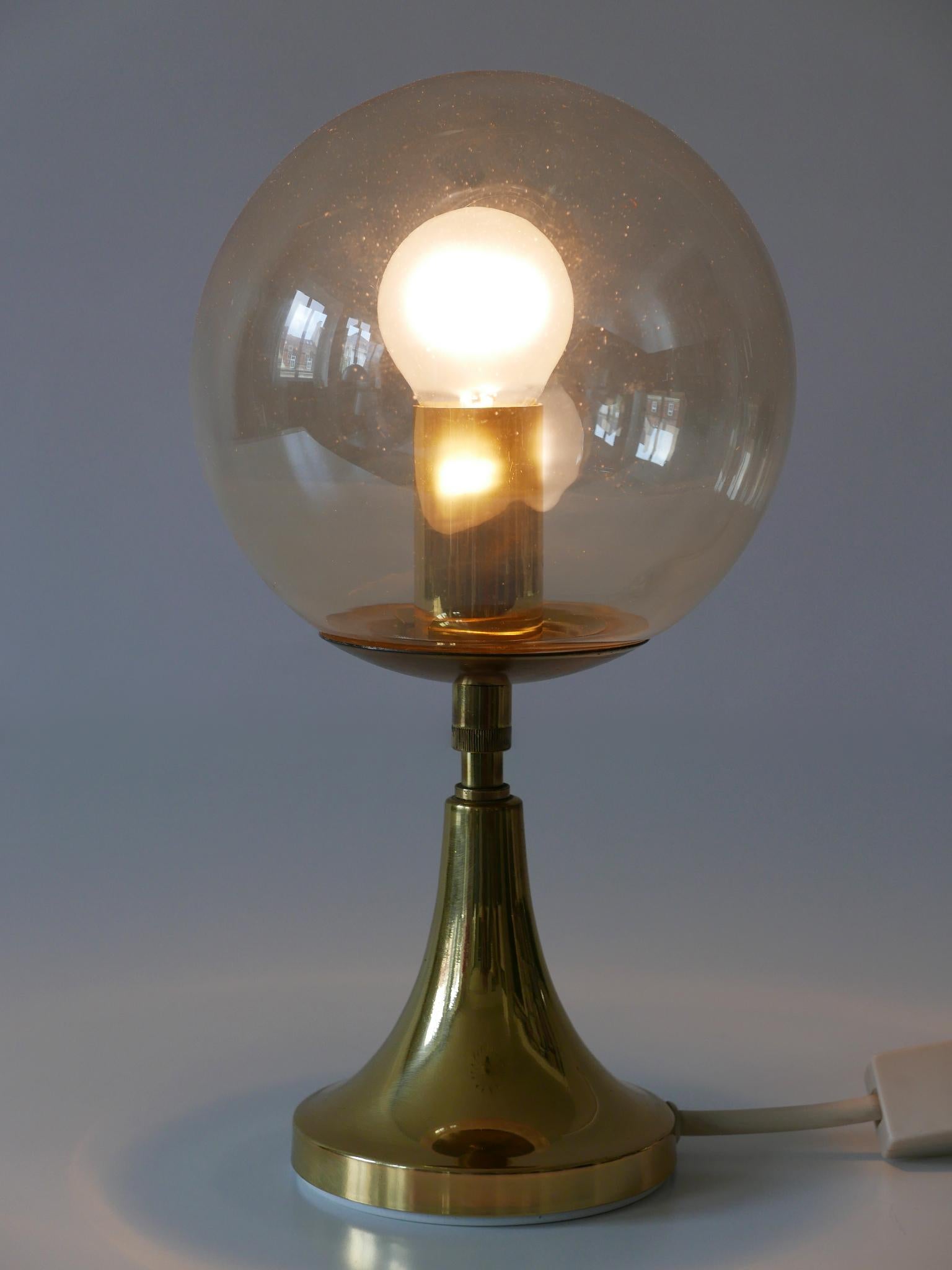 Elegant Mid-Century Modern table lamp. Manufactured by Sölken Leuchten, Neheim-Hüsten, Germany, 1960s.

Executed in brass and glass, the lamp comes with an E14 / E12 Edison screw fit bulb socket, is in working condition and runs both on 110 and