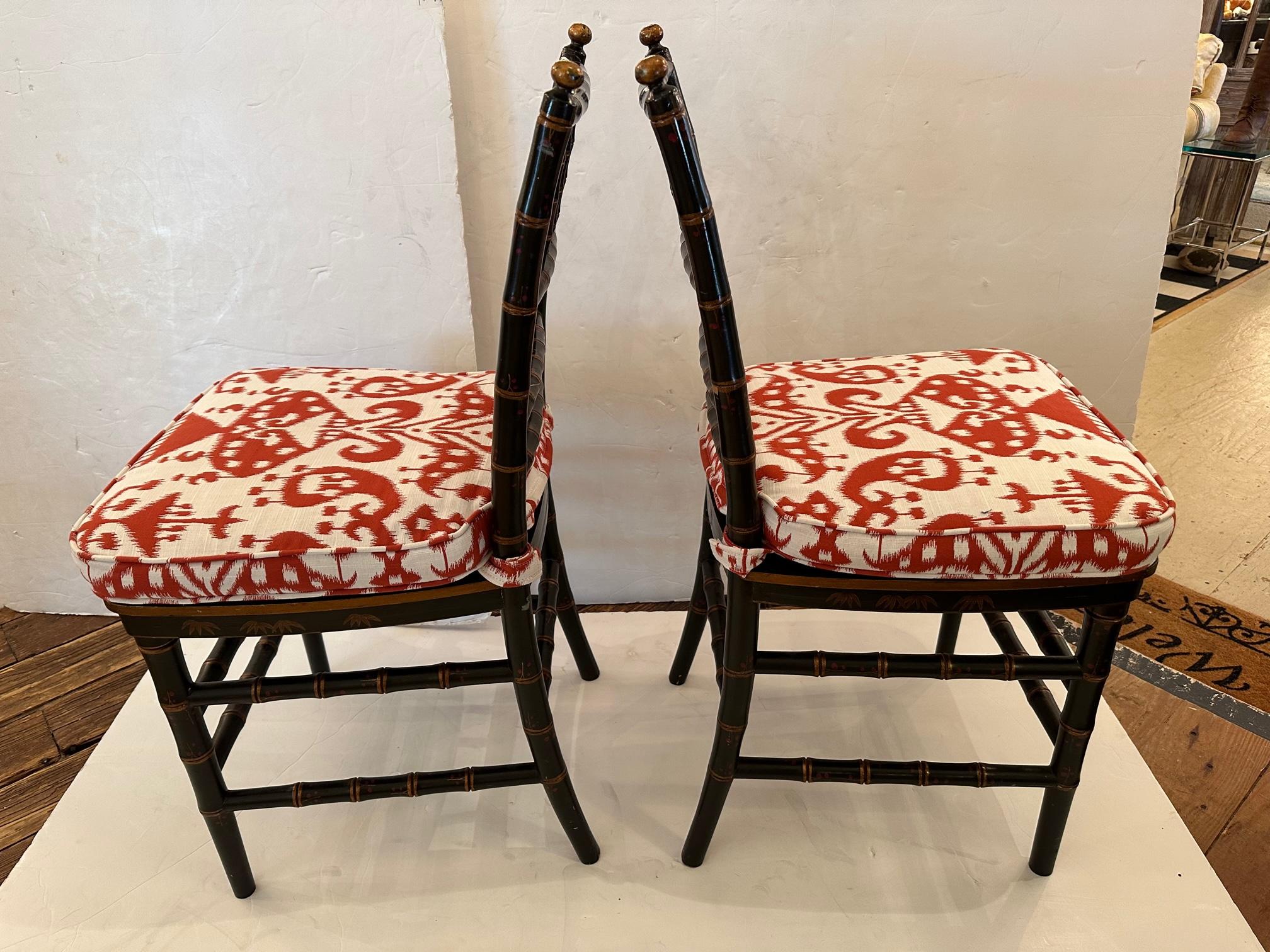 Lovely pair of black faux bamboo side chairs having hand painted decoration and newly upholstered seats.  The red and white fabric contrast and complement the colors of the wood.