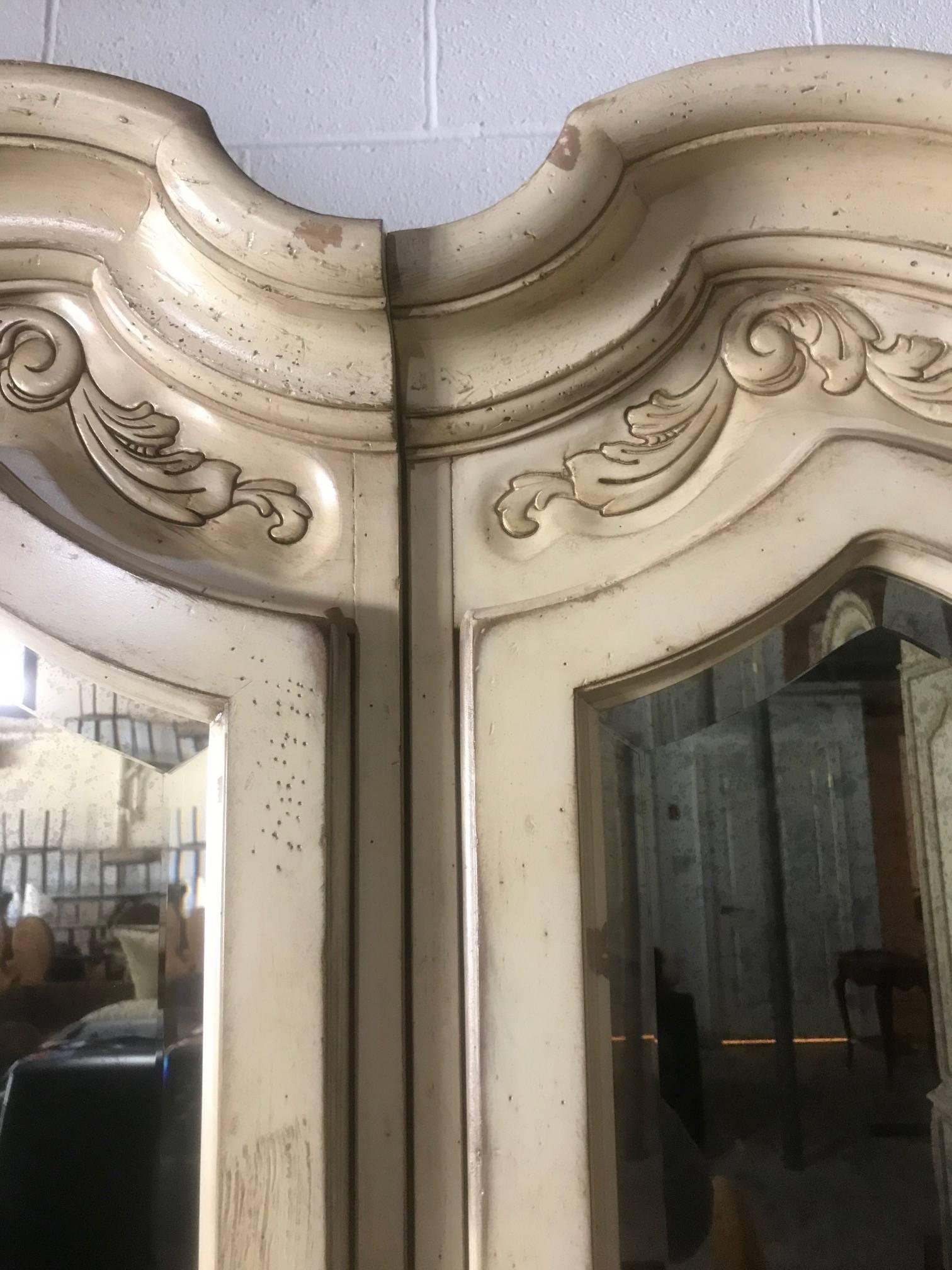 A romantic pair of century Cantal armoires having mirrored doors, carved wood decoration at the top with adjustable shelves inside, and painted a special cream antiqued Biscay. We are selling them as a pair, but they also have the large armoire that