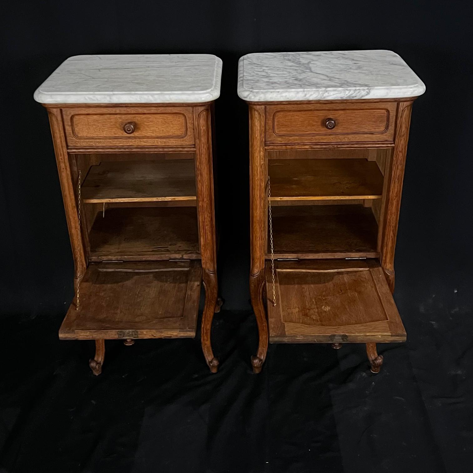Lovely antique pair of oak French night stands, bedside tables or side tables. Made of oak featuring one drawer over a cabinet with two shelves, one removable. Lovely cartouche carvings and cabriole legs lead to scrolled feet. Versatile and useful