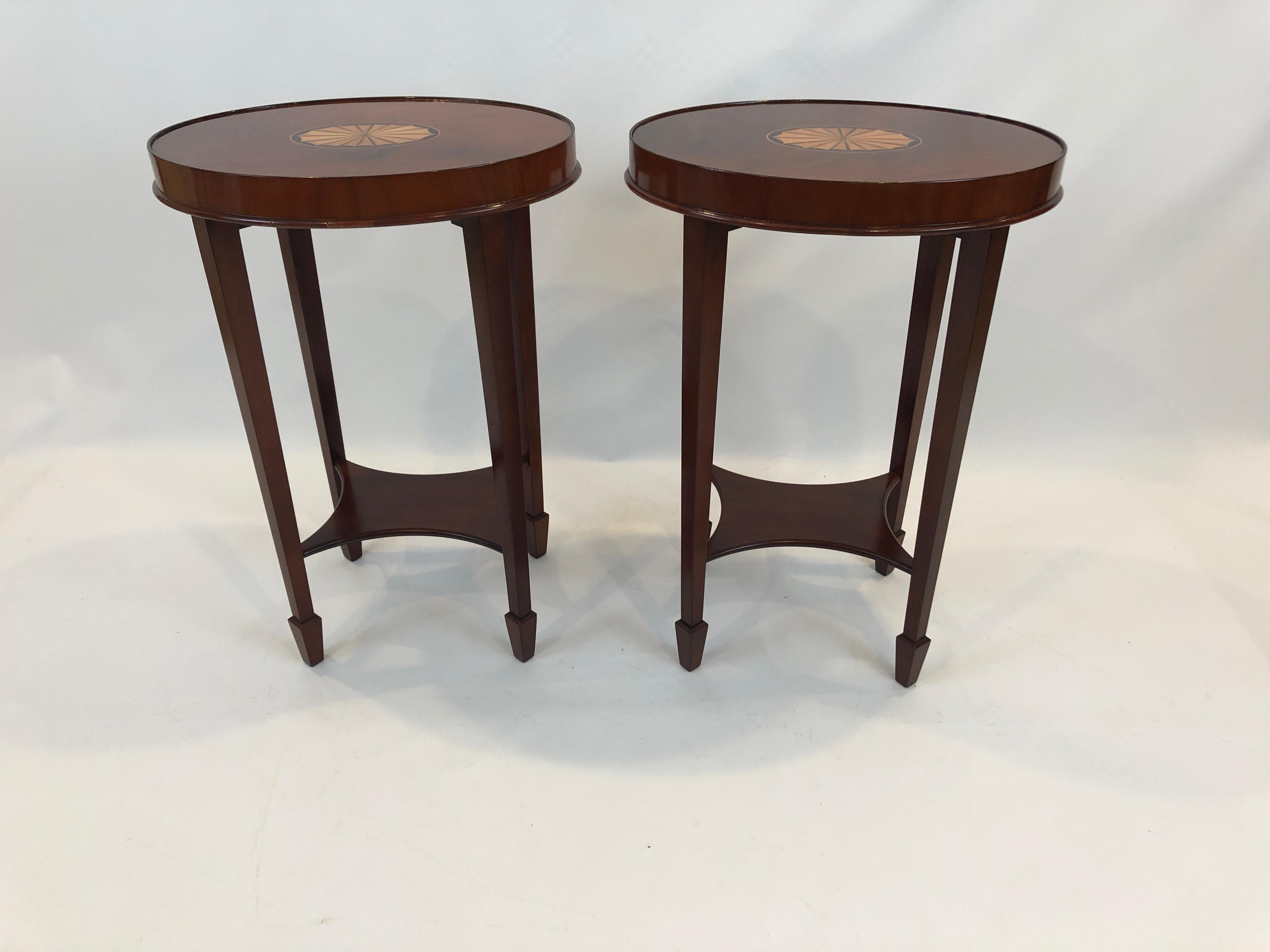 A gorgeous pair of flame mahogany oval side or end tables having ebony and satinwood central fan inlays, small bottom tier and handsome tapered legs with arrow shaped feet.