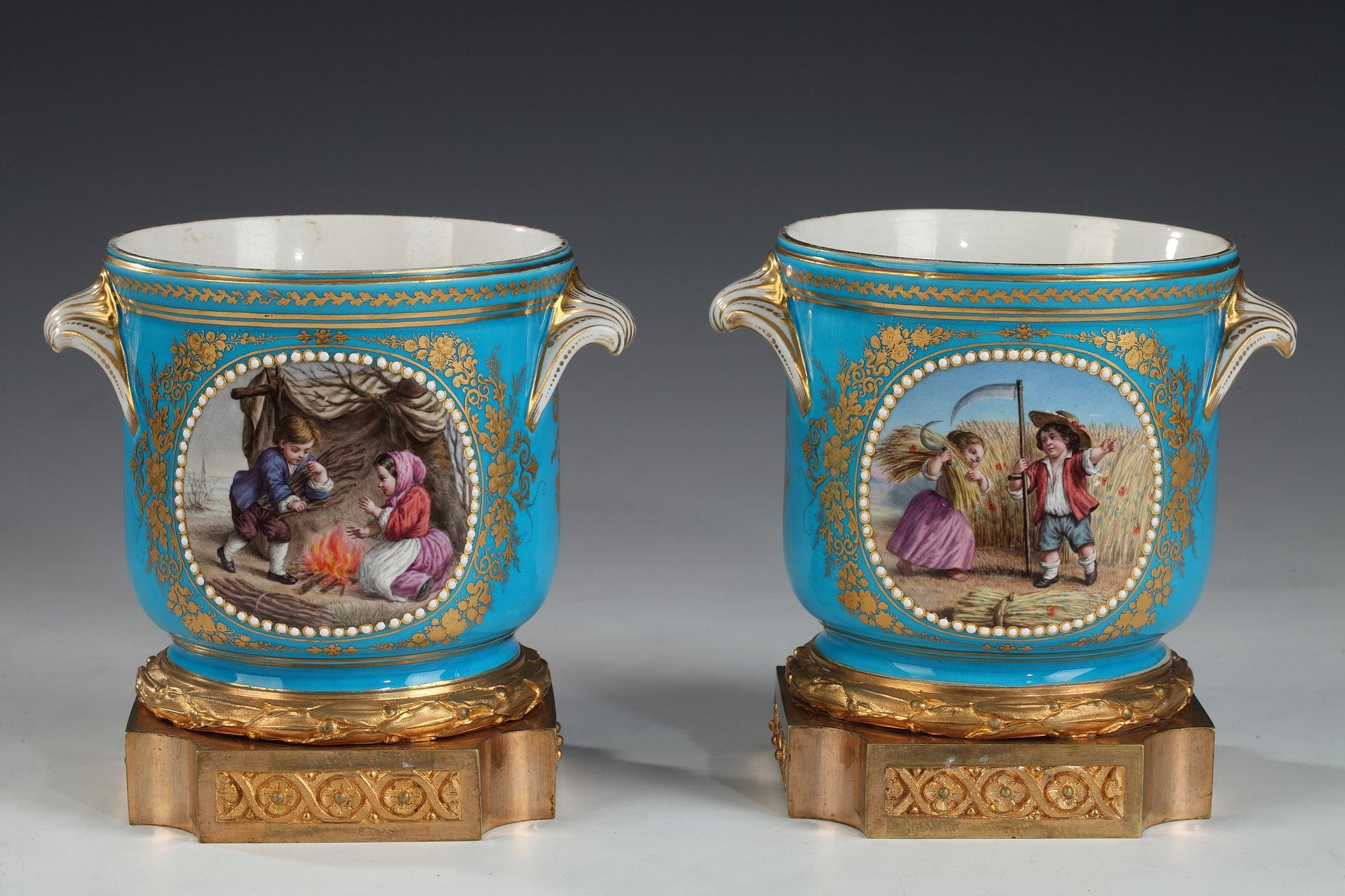 Pareja de enfriadores de vidrio de porcelana con medallones pintados y adornos dorados sobre fondo azul turquesa, montados sobre una base de bronce dorado, al estilo de la Manufactura de Sèvres. En el anverso hay dos escenas pintadas de la infancia