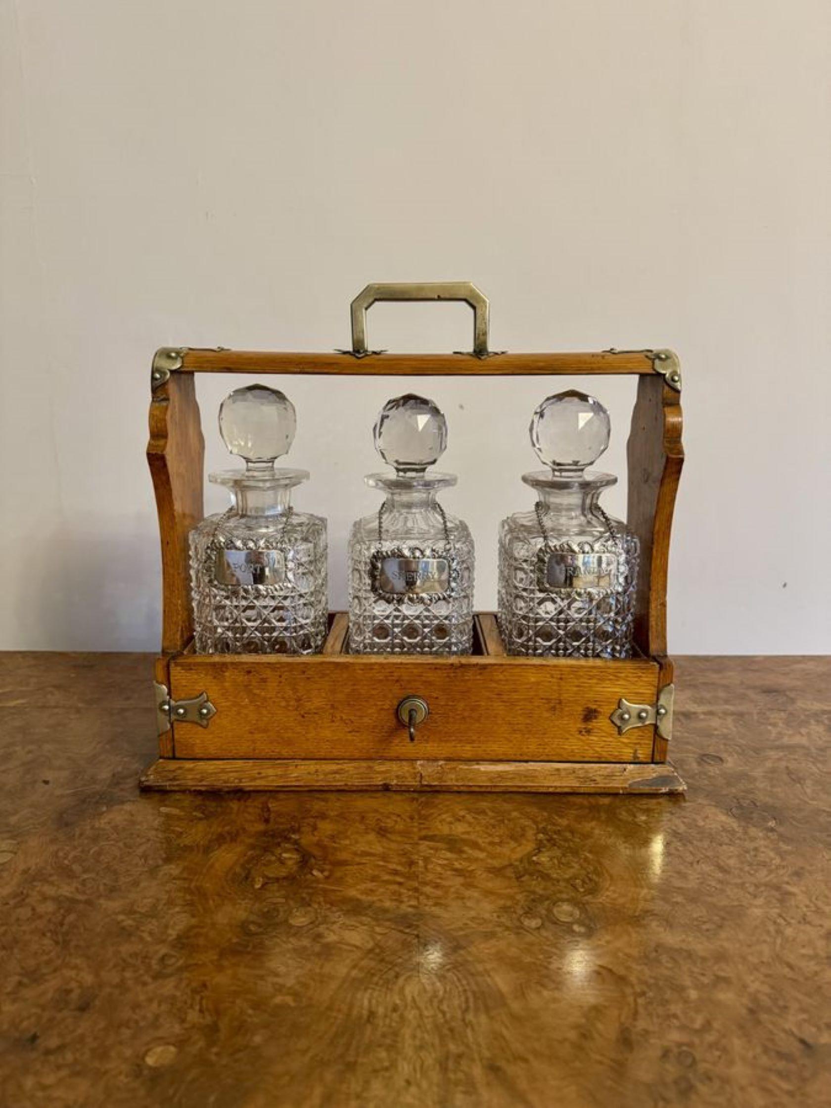 Precioso tantalio antiguo de roble eduardiano de calidad, con monturas de latón y asa de transporte de latón en la parte superior, con un panel frontal que se abre con llave y deja ver tres decantadores de cristal tallado con etiquetas plateadas