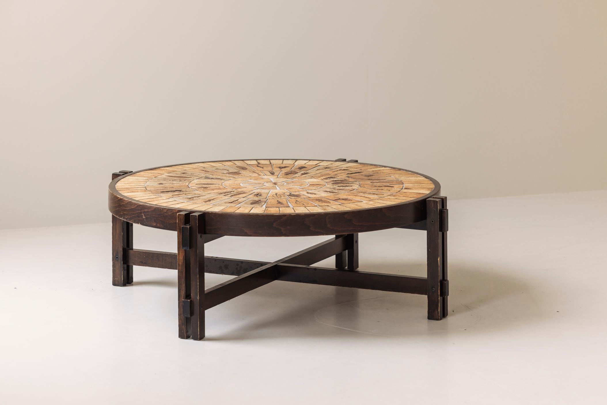 Lovely round coffee table by Roger Capron, France 1960s. This piece features a beautifully stained wooden frame and a tabletop adorned with glazed ceramic sandstone tiles, each carefully decorated with botanical motifs. Presented in its original and