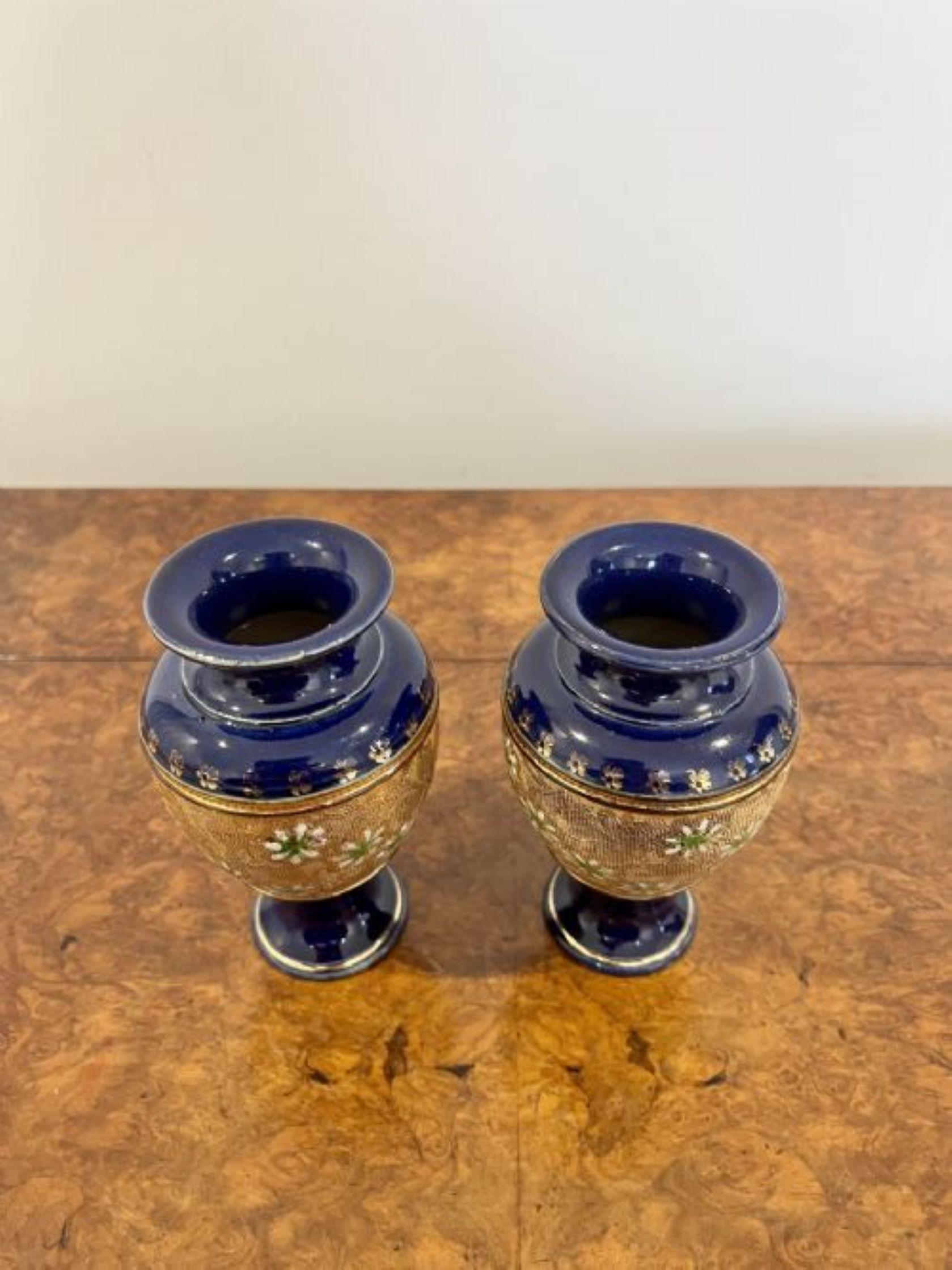 Lovely small pair of antique Victorian Royal Doulton vases having a lovely pair of small antique Royal Doulton vases having a band of green and white flowers on a golden background to the centre of the vase and a dark blue glaze with gold decoration
