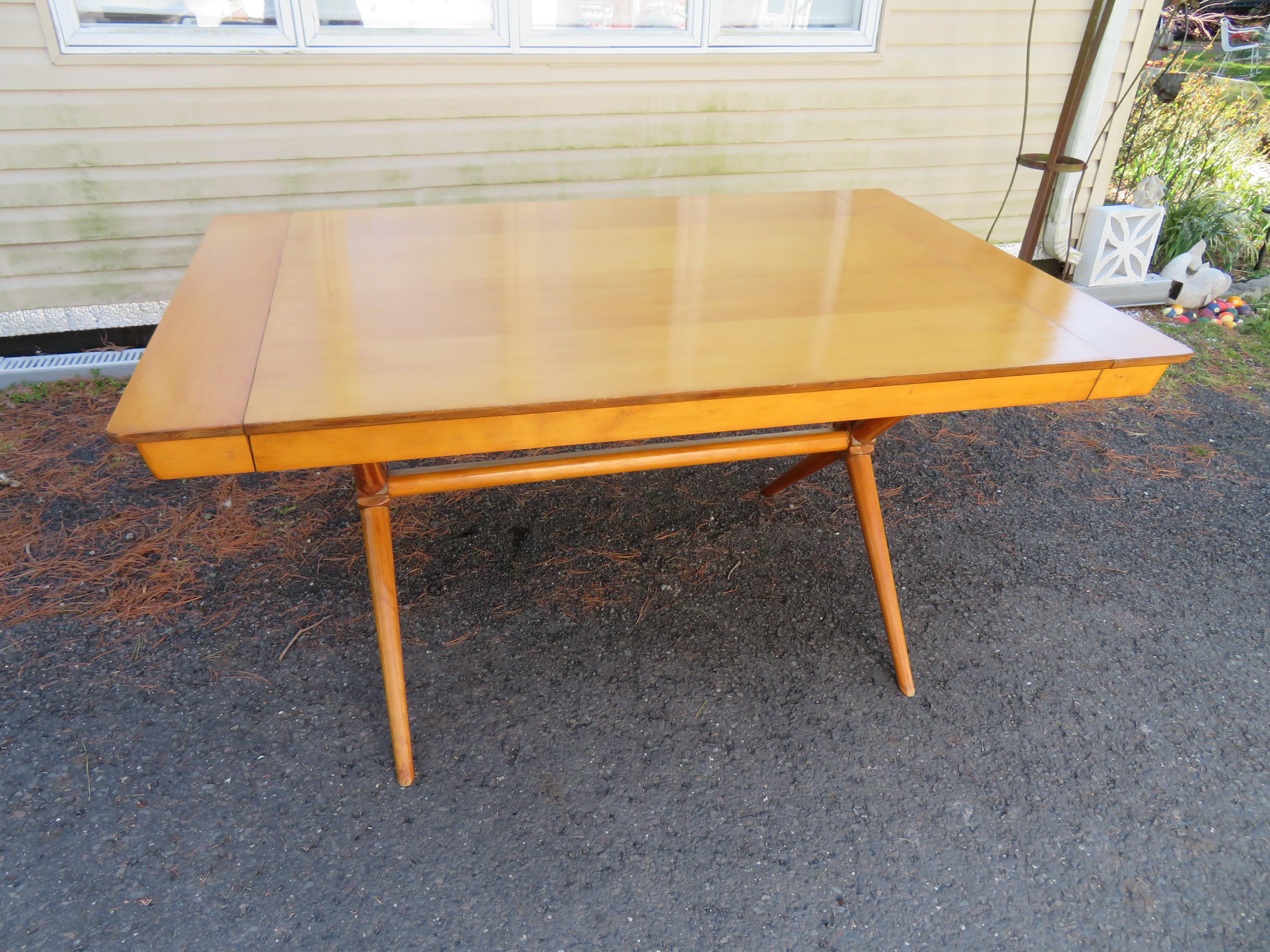 Lovely maple dining table with an X base in the style of Robsjohn Gibbings. We love the unusual way the leaves are added to the ends of the table instead of the middle. Comes with 2-10? leaves. This table measures 30