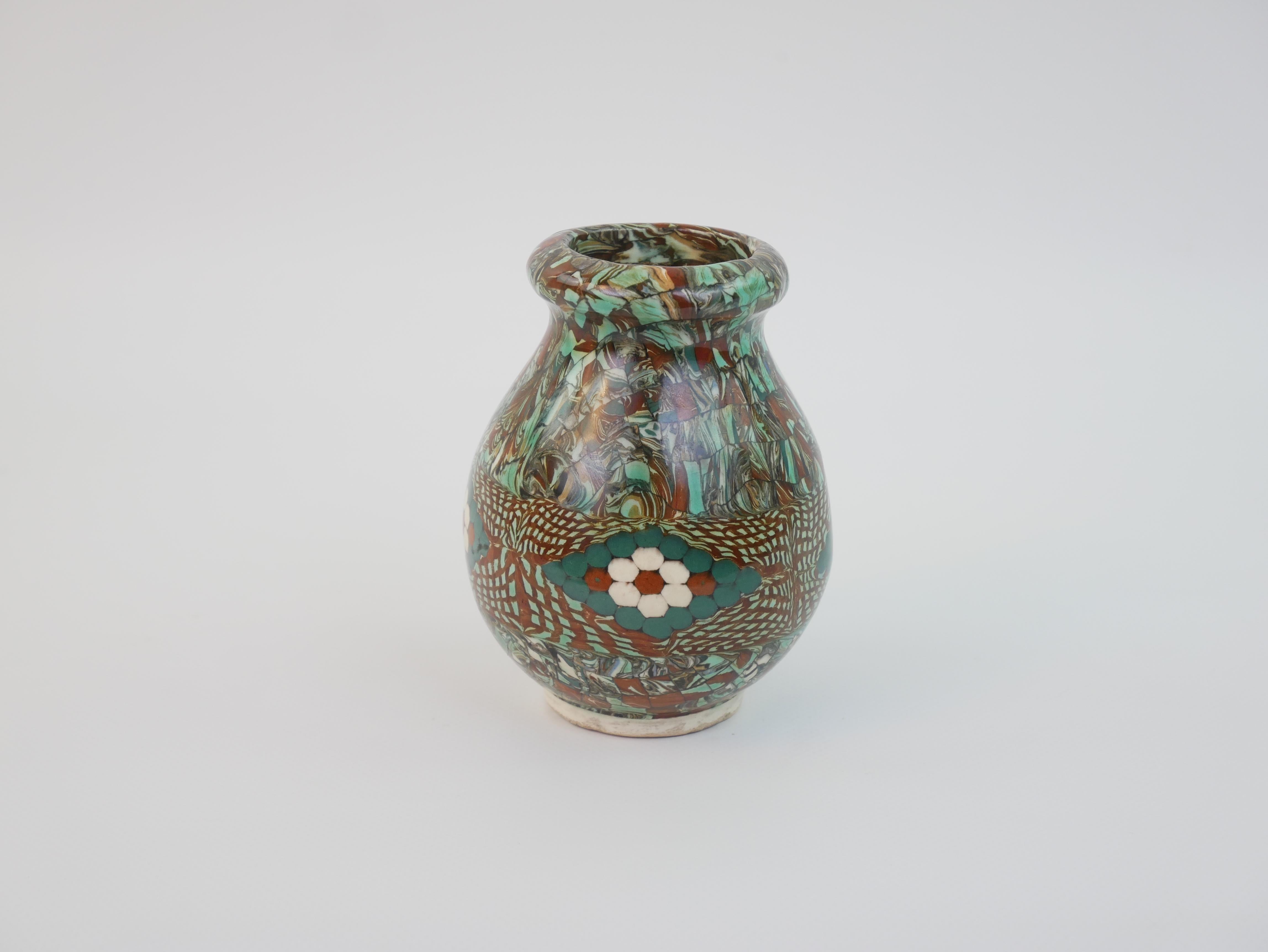 Questo piccolo vaso di Jean Gerbino, creato negli anni '30, è uno splendido esempio della sua innovativa tecnica del mosaico. La sua forma arrotondata presenta intricati motivi realizzati con intarsi di argilla colorata, che formano un'armoniosa