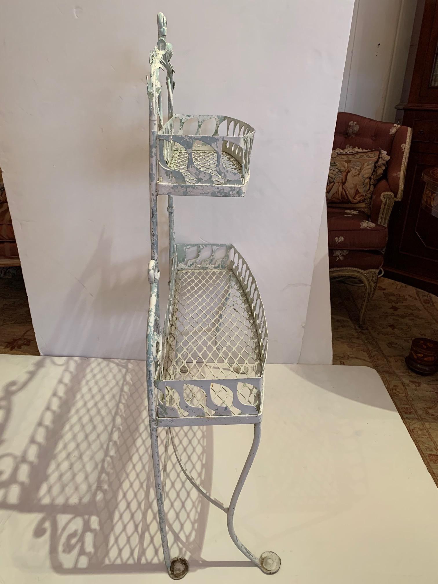 Charming painted metal two-tier plant stand having a white and light green distressed finish with decorative curlicues and galleries. Great indoors or on the deck, for plants or other collections.