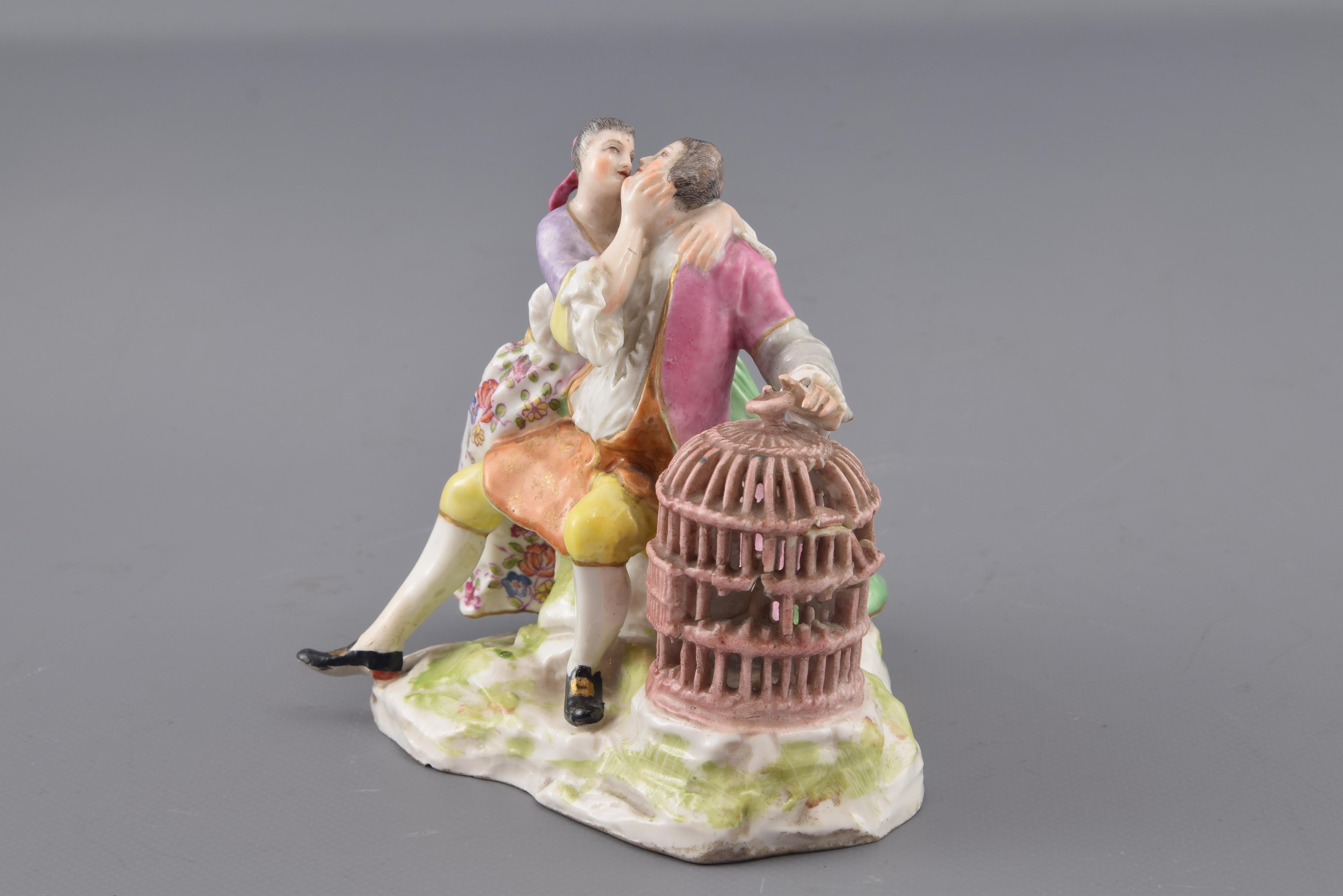 Courtesans and cage. Glazed porcelain. Model Johann Joachim
Enameled porcelain figurine with base resembling rocks and a couple of lovers dressed in the manner of the 18th century, with the boy extending his left hand towards a large bird cage. The