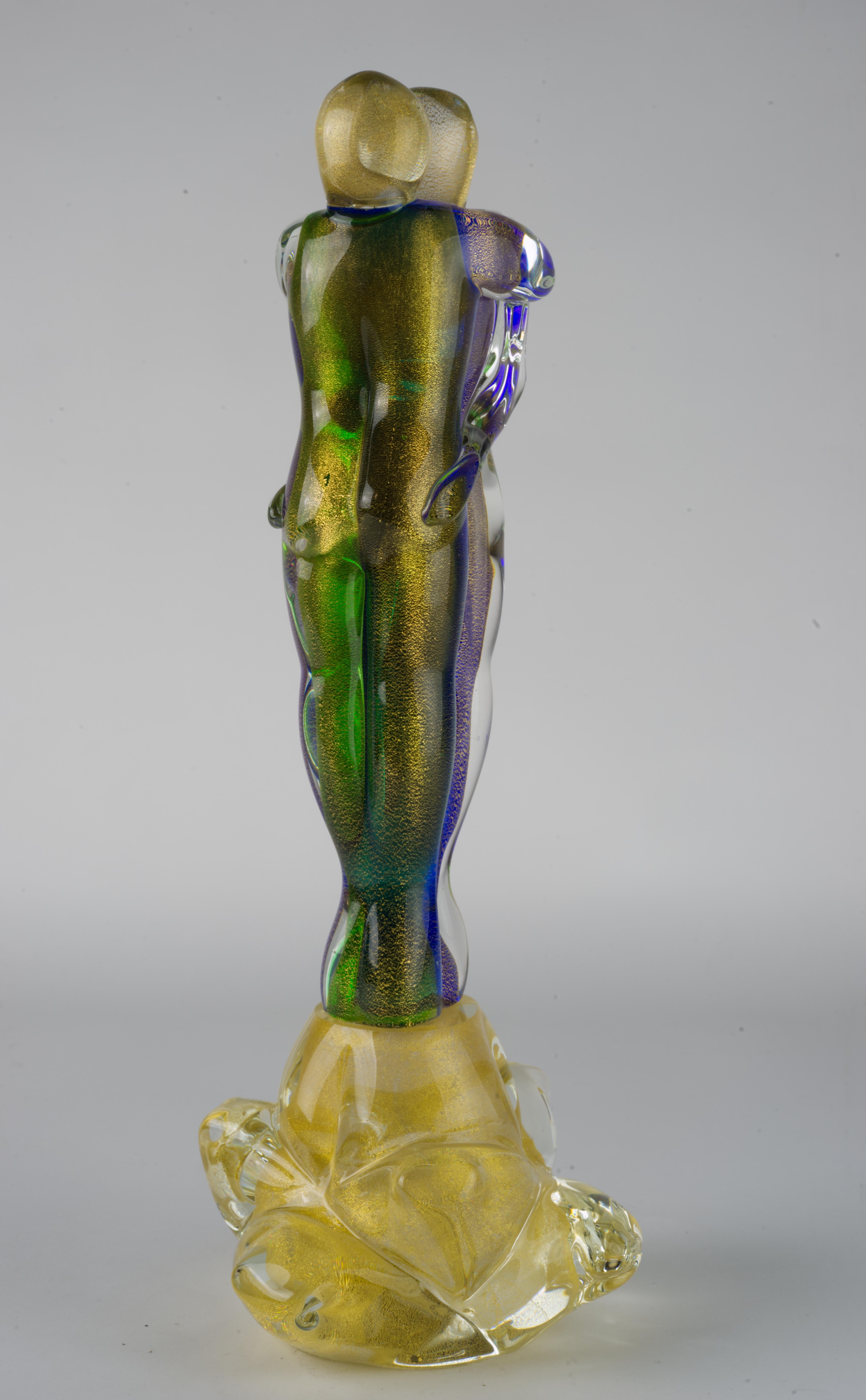 Abstrakte Murano-Glasskulptur von zwei Liebenden, die sich umarmen, aus grünem, violettem und klarem Glas mit Goldflockeneinschlüssen, umhüllt von klarem Glas in Sommerso-Technik. Die beiden Figuren werden von einem figurativen Sockel aus Klarglas
