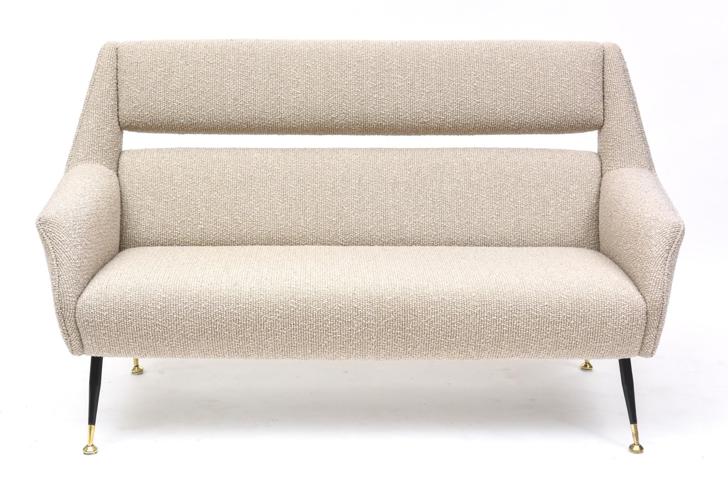 A quintessential 1950s Mid-Century Italian loveseat by Gigi Radice for Minotti, upholstered in a luxe wool boucle by Beacon Hill, perched on black enameled steel legs with with polished brass feet. Ciao, bella!