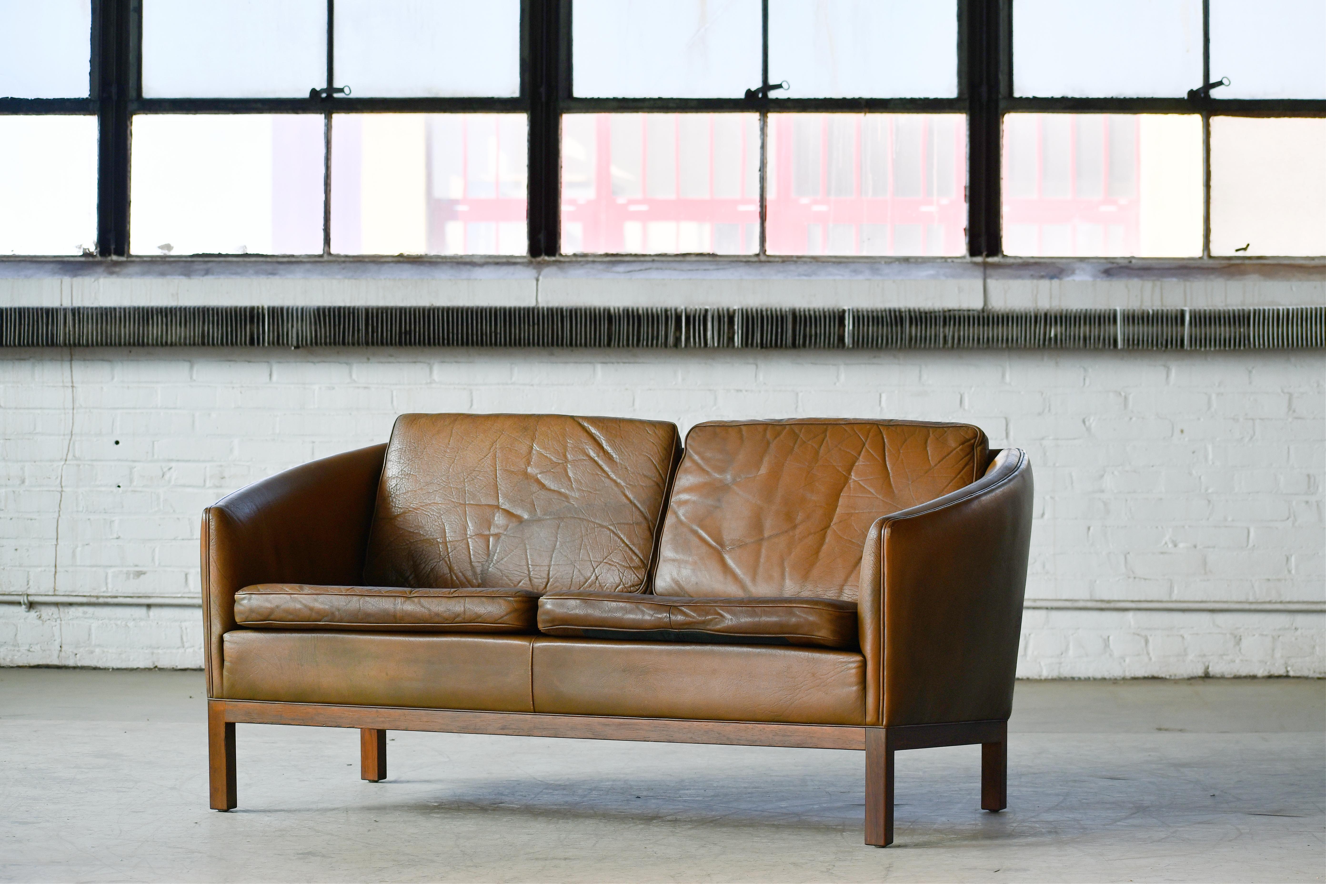 Classic Danish Illum Wikkelso designed sofa in a light brown Buffalo leather. Raised on a base of rosewood giving the sofa richness and elegance.  The perfect relaxed look of the 1960's probably made around late 1960's to sometime in the 1970's.