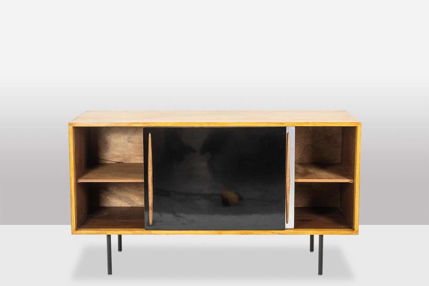 Buffet bas en frêne blond ouvrant avec deux portes coulissantes, l'une en aluminium brossé et l'autre en stratifié noir, la base droite en métal laqué noir et les poignées triangulaires.

Œuvre réalisée dans les années 1960.

Dimensions : H 77,5 x L