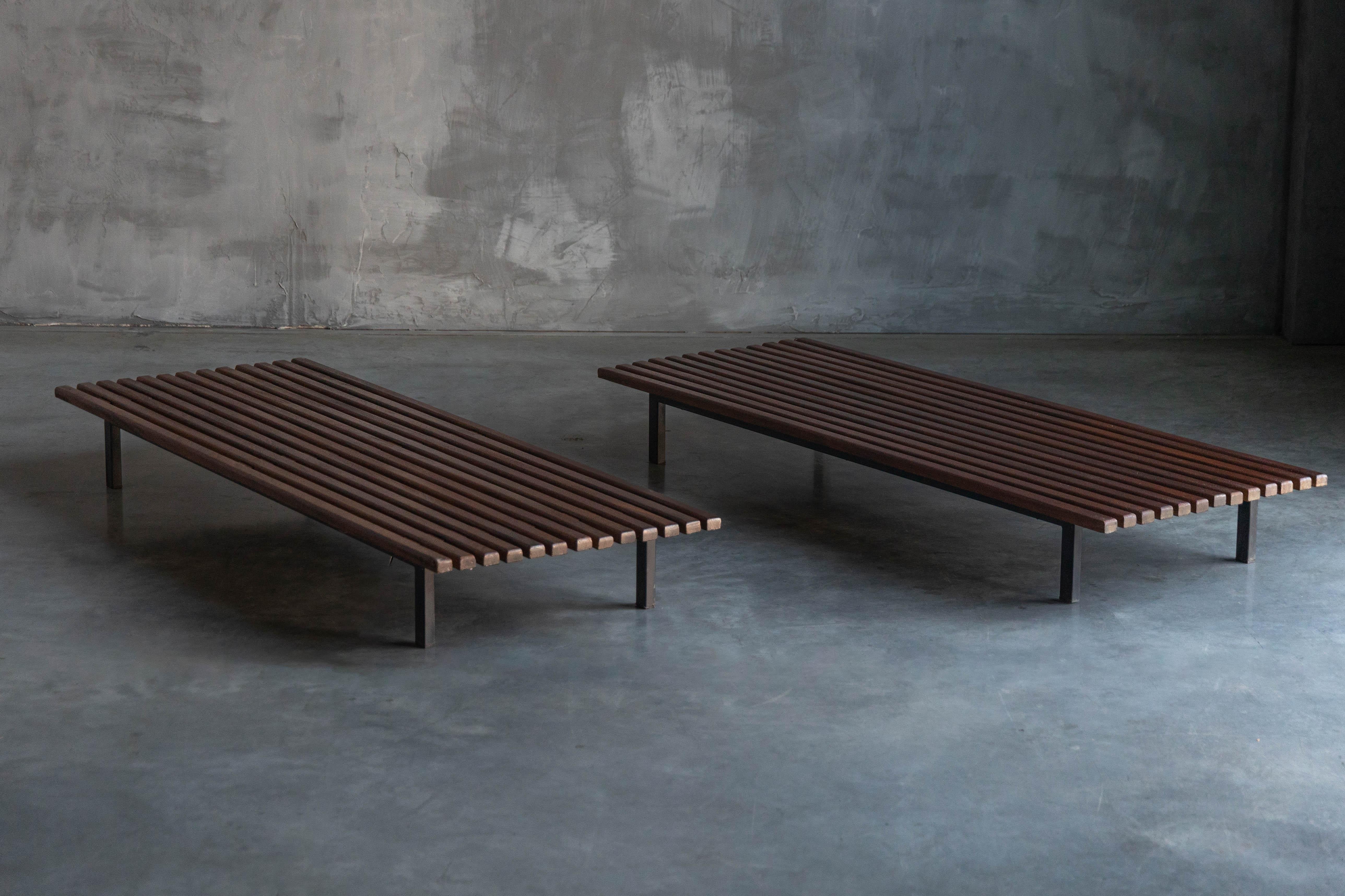 This Cansado Bench, designed by Charlotte Perriand in 1954, is crafted from solid oak with an enameled steel base, balancing warmth with industrial strength. The parallel wood slats create a rhythmic, architectural presence, while the patinated