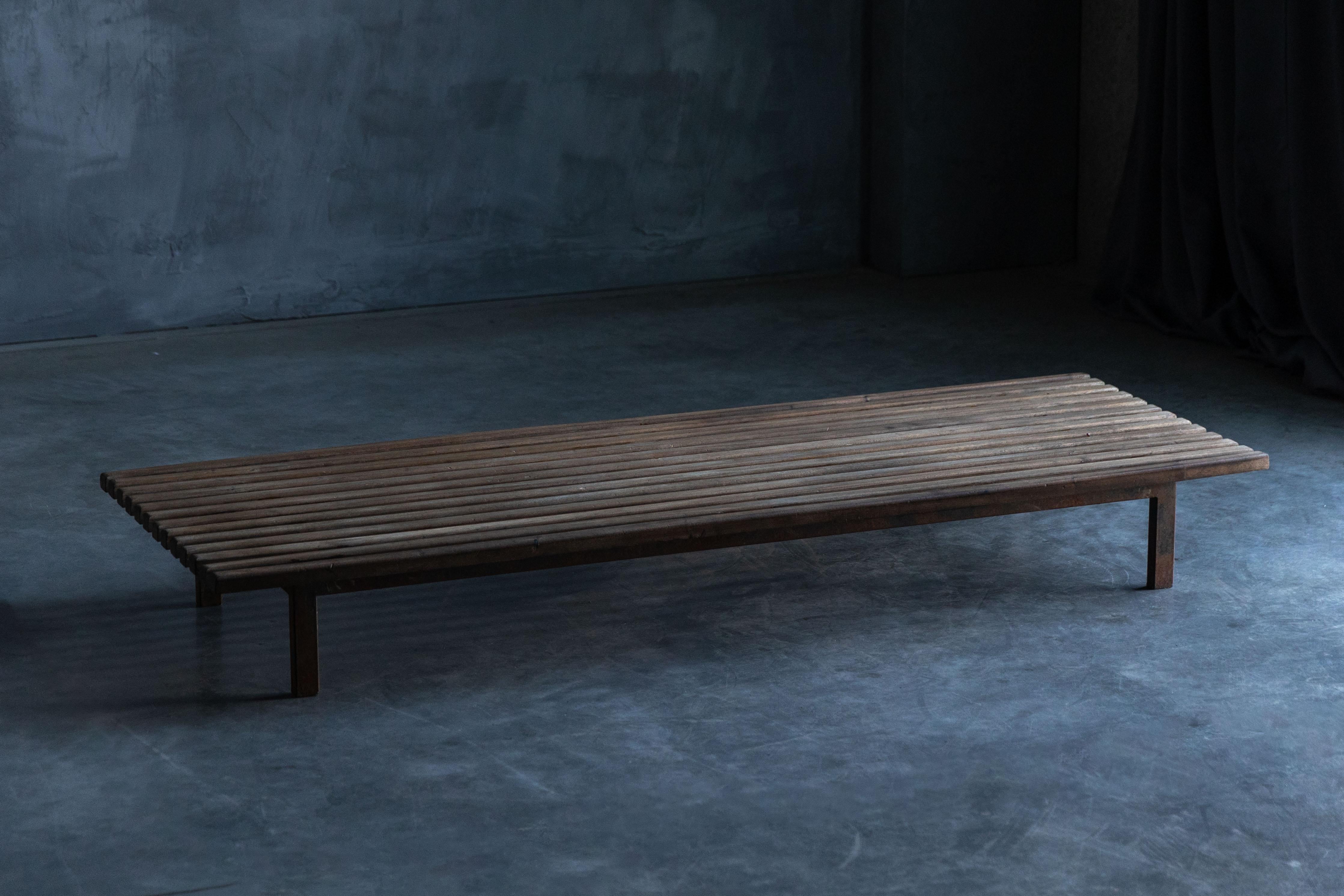 This Cansado Bench, designed by Charlotte Perriand in 1954, is crafted from solid oak with an enameled steel base, balancing warmth with industrial strength. The parallel wood slats create a rhythmic, architectural presence, while the patinated