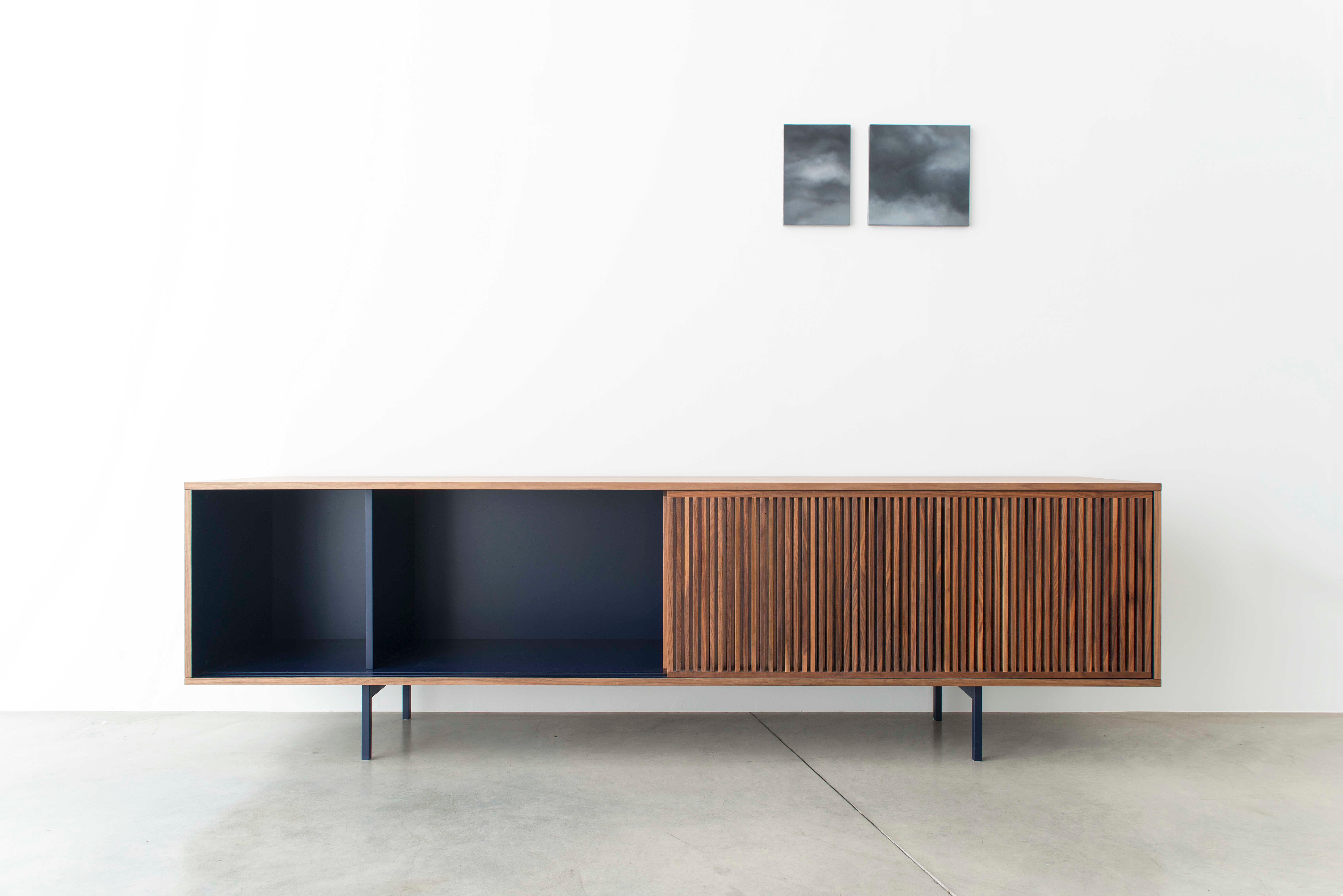 A rectangle with clean, extremely linear shapes, which expresses an essential refinement: the low sideboard is a container in black walnut wood, which hides dark, lacquered shelves and all inside part.
On the front, doors with vertical battens