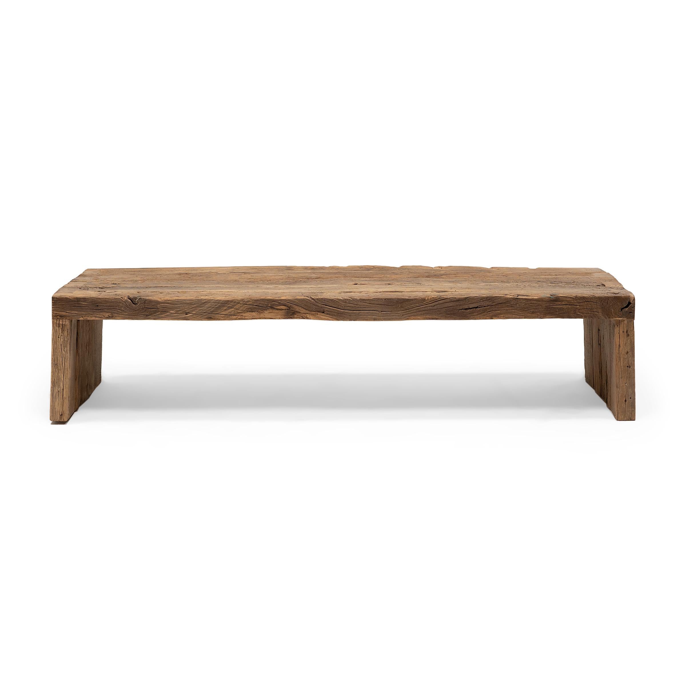 Cette table basse artisanale est une célébration du style wabi-sabi. Fabriquée en bois d'orme épais récupéré de l'architecture de la dynastie Qing, la table présente un design minimaliste en cascade et est laissée brute pour préserver la beauté