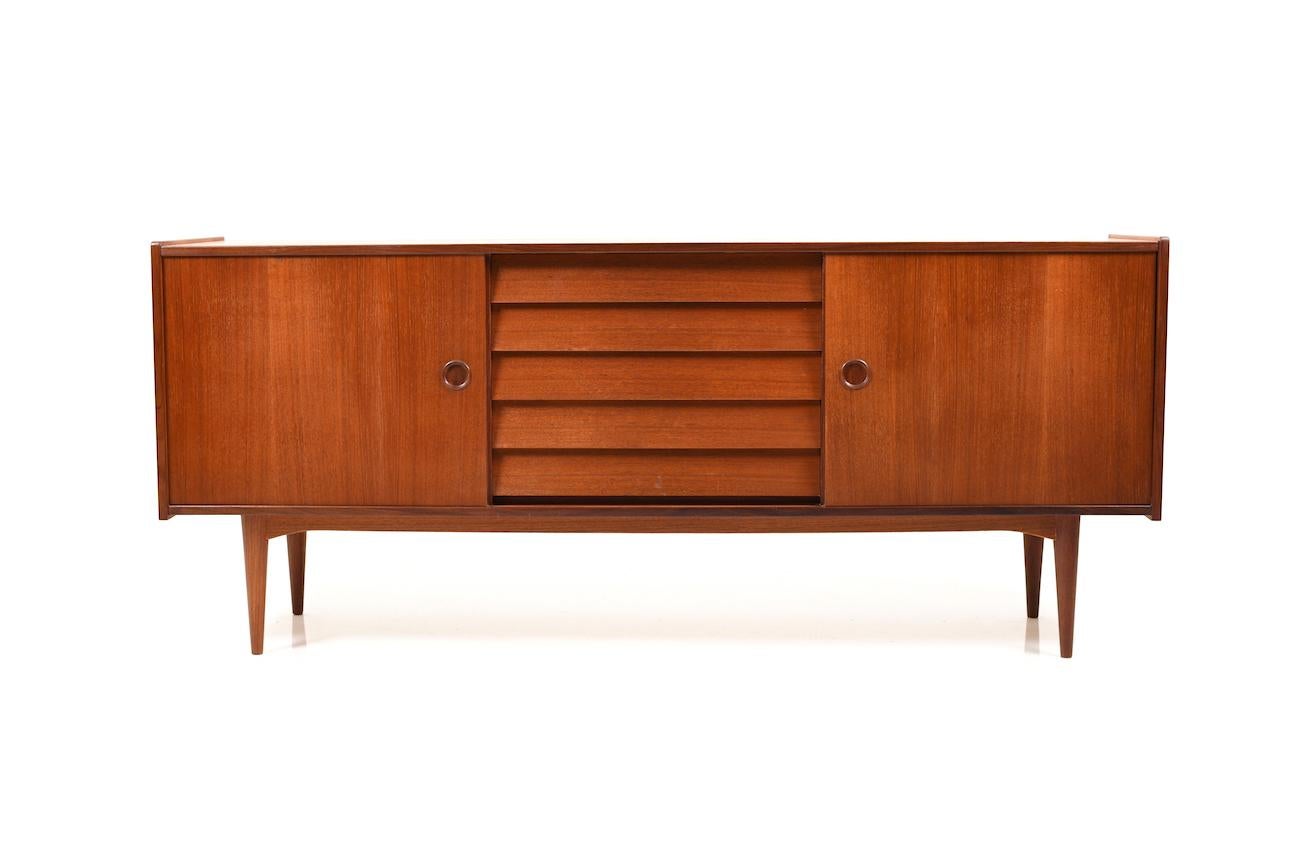 Midcentury Danish teak wooden sideboard. Designed by Nils Jonsson for Troeds. Front with five drawers and two sliding doors. Behind the sliding doors with shelves.