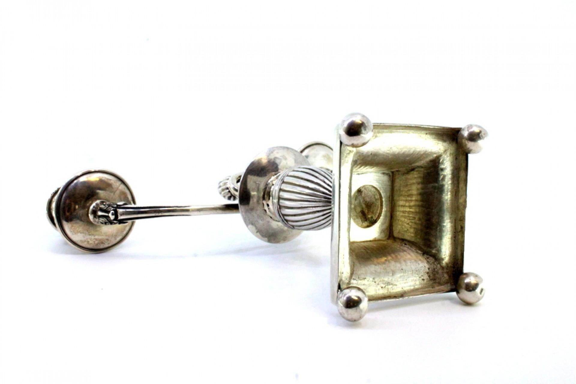 Description : Candélabre bas en argent cannelé à deux lumières, base carrée reposant sur quatre pieds sphériques et pommeau surélevé. Métal : Argent. Origine : Portugais. Poinçon : aigle debout. Poids : 487,78 grammes. Dimensions : 20cmx22cm.