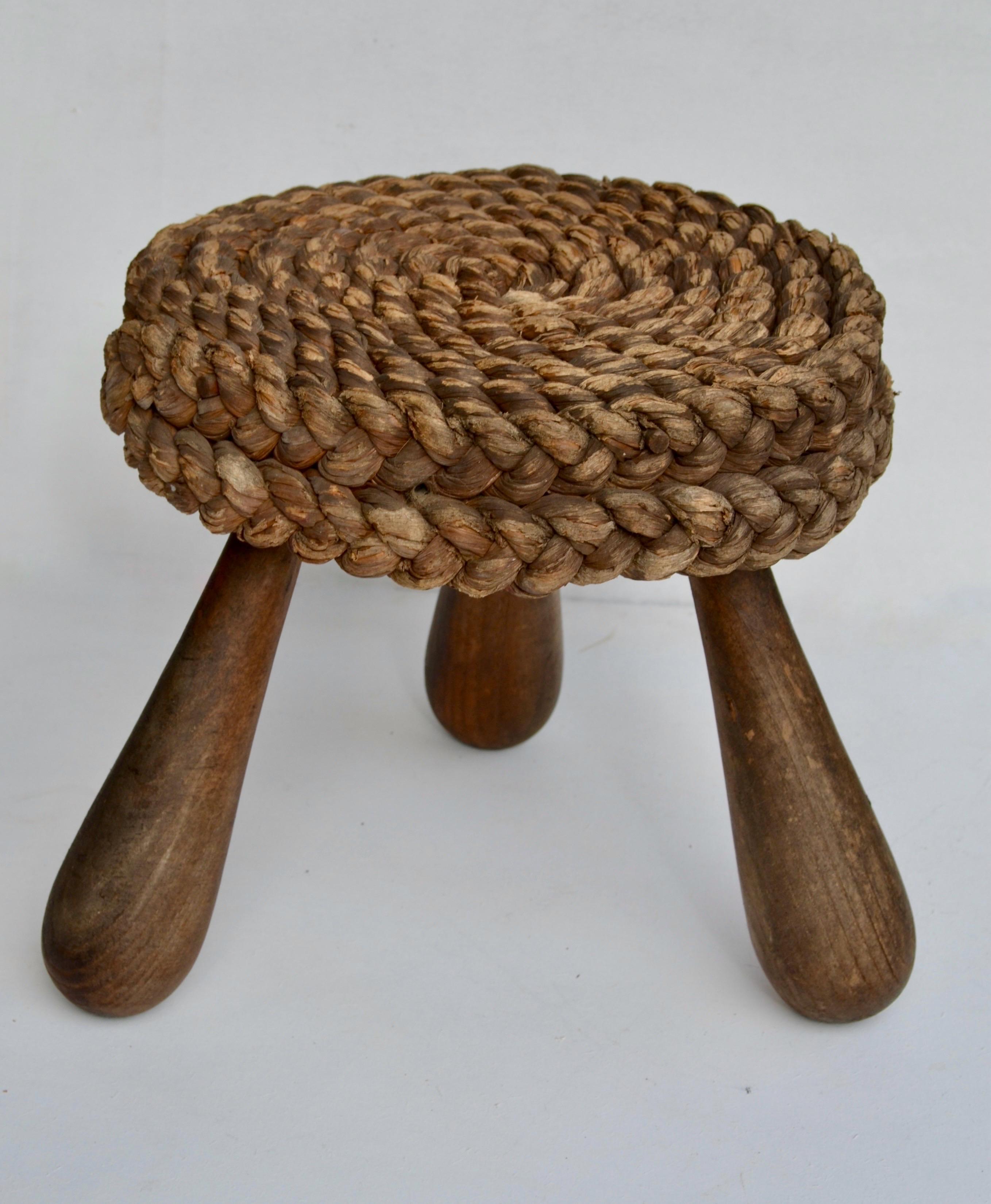 Charming mid-century French low stool designed by Adrien Audoux and Frida Minet. This rustic piece features a circular seat intricately handwoven in natural raffia/rattan, resting on three sturdy oak legs with a sculptural tripod base. A fine