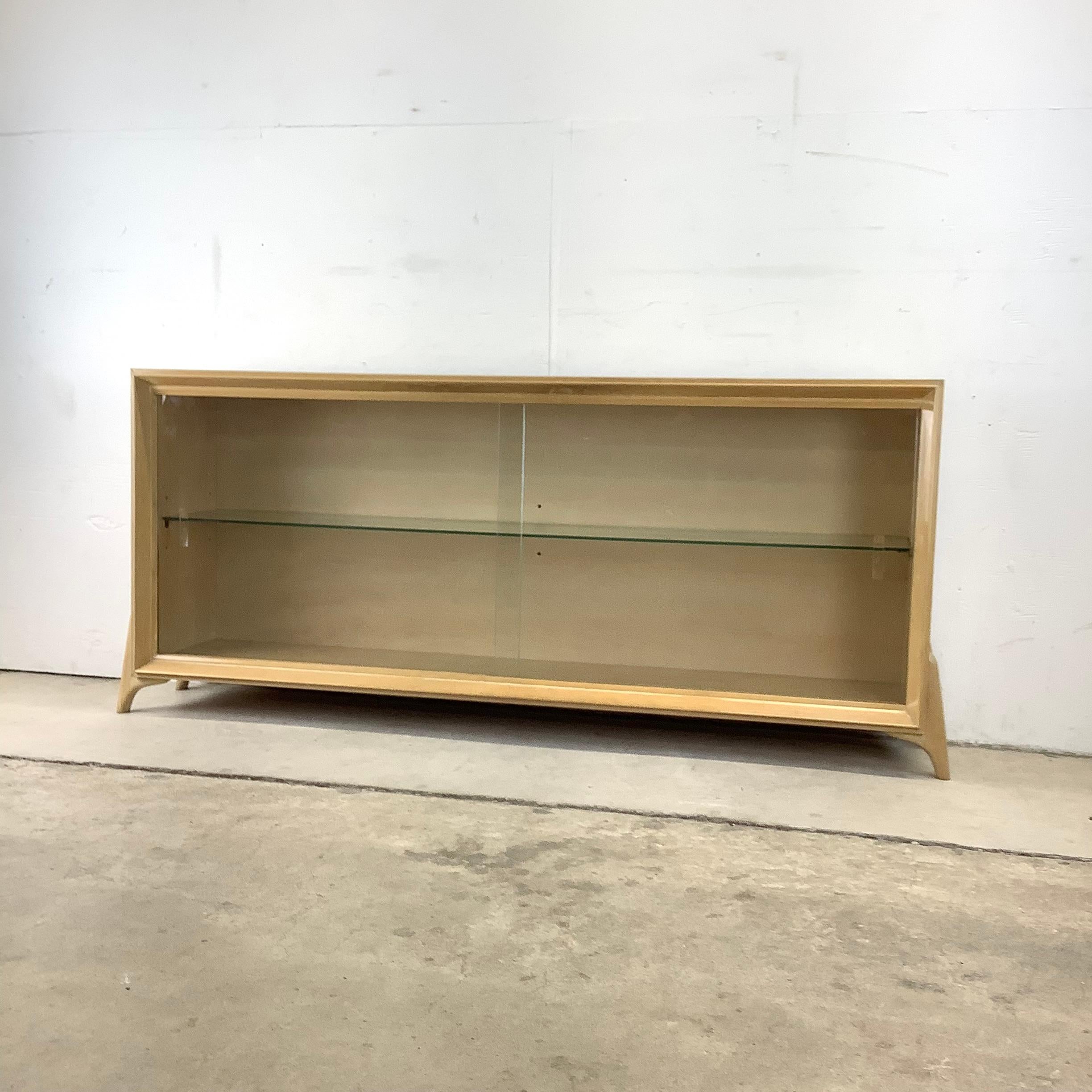 This uniquely sized mid-century bookcase features sturdy vintage blonde wood construction with lacquer finish and adjustable glass shelf. Sliding glass doors add to the display case quality of this low bookcase while the clean modern lines and