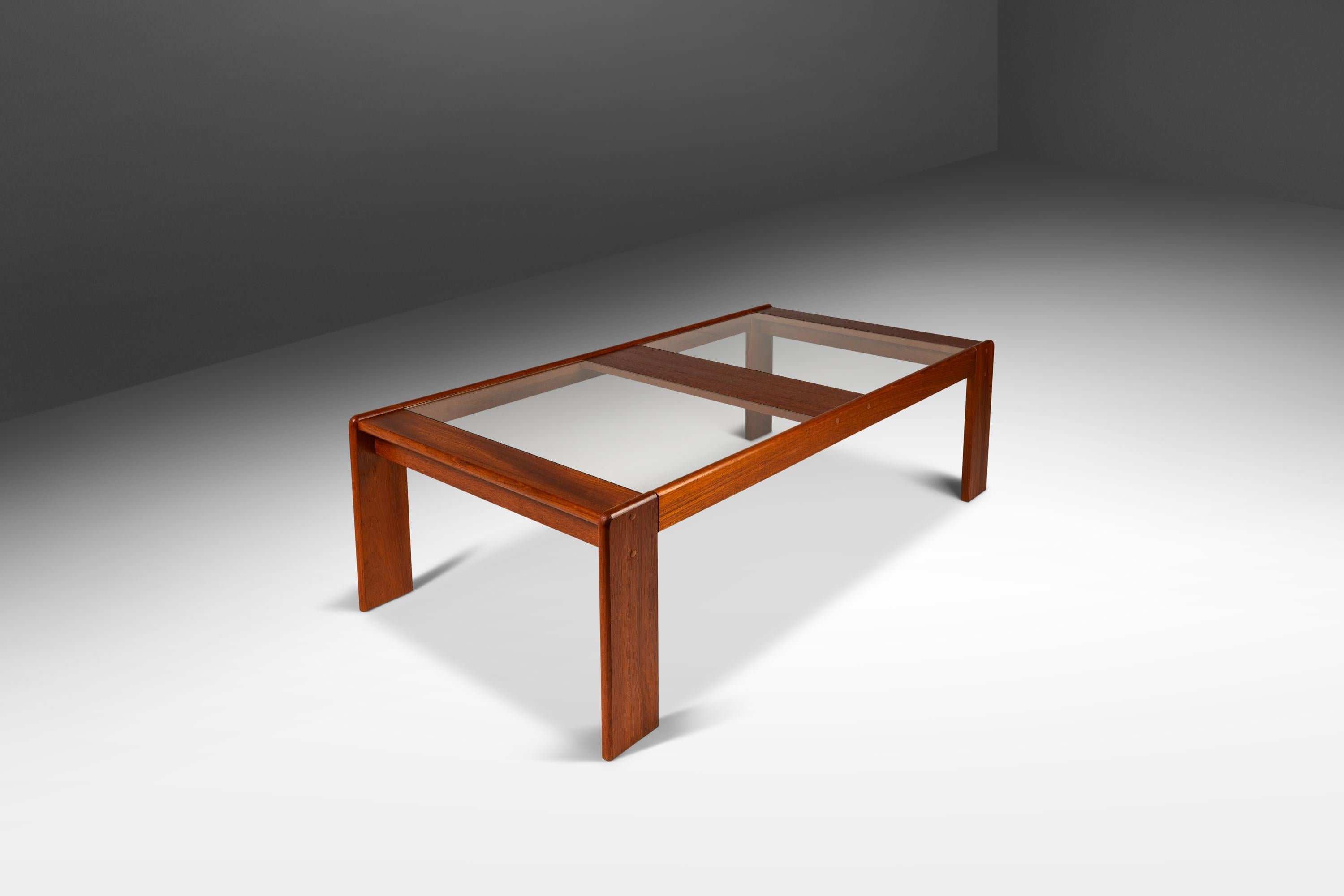 Voici une étonnante table basse de fabrication danoise, aussi rare qu'esthétiquement attrayante. Construite à partir d'un cadre en teck massif de Birmanie aux veinures vibrantes et surmontée de deux panneaux de verre, cette table est à la fois