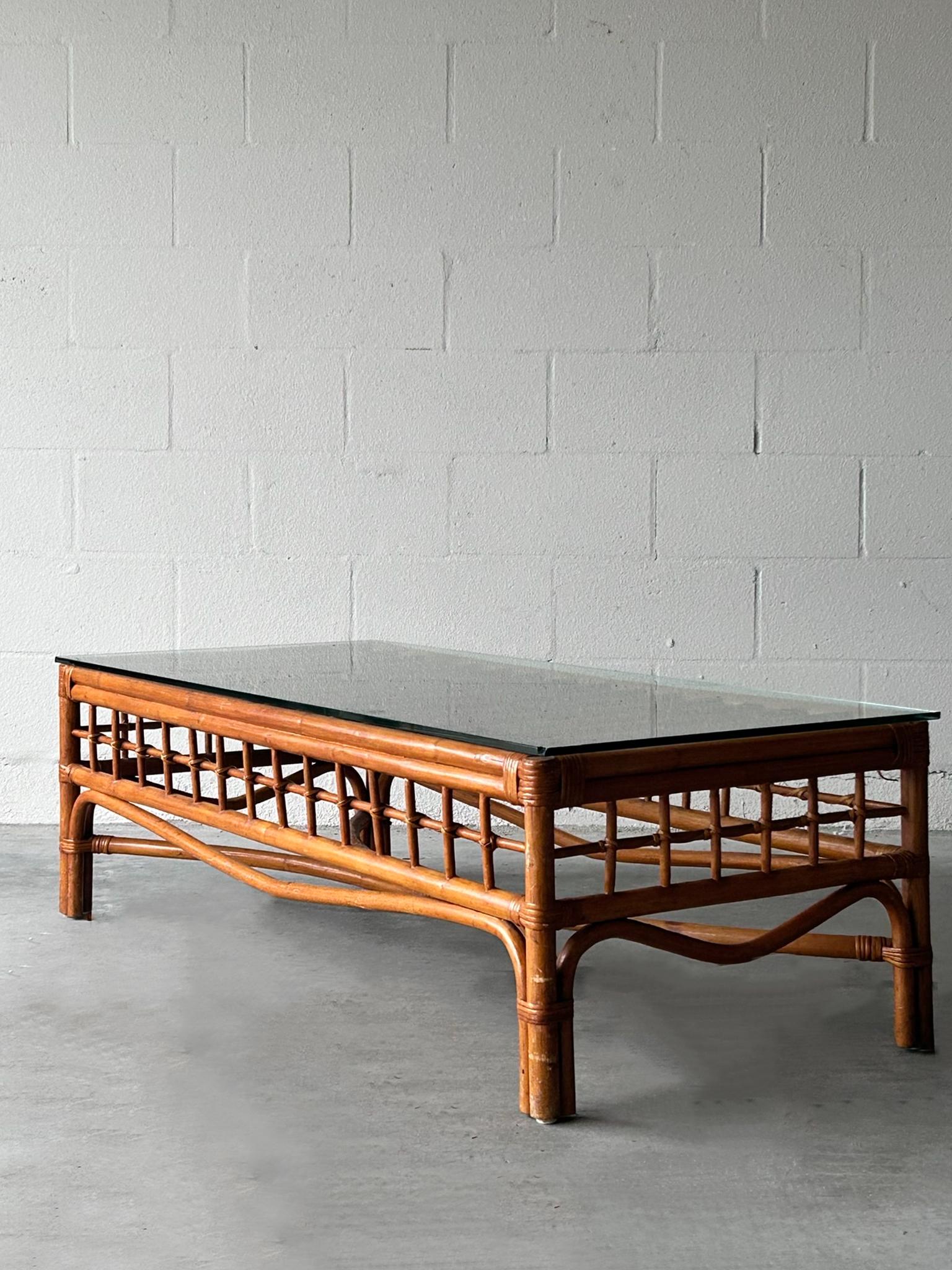 Une belle table basse vintage en bambou avec un cadre tissé robuste et un plateau en verre transparent. Les détails complexes en rotin ajoutent de la texture et de la chaleur, ce qui convient parfaitement aux intérieurs bohémiens, côtiers ou du