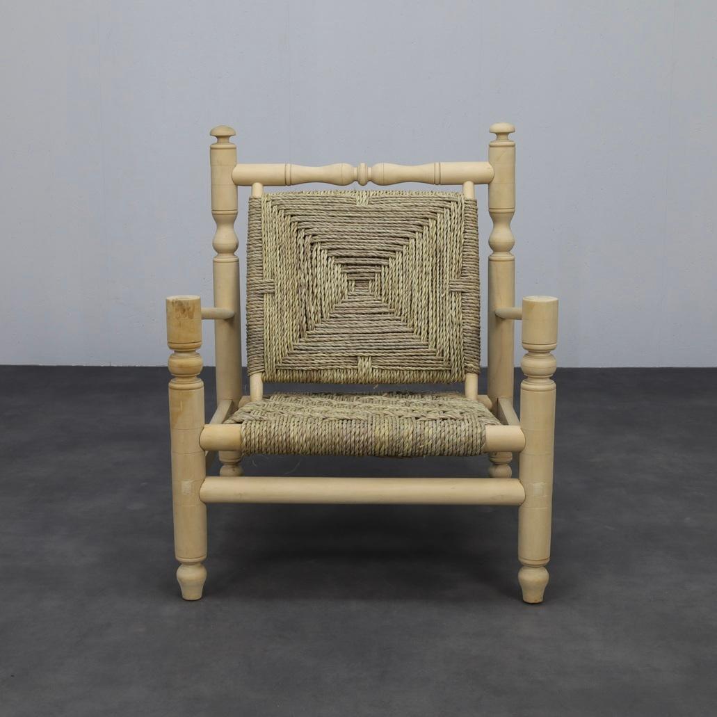 Un sillón bajo escultural en el espíritu de Adrian Audoux y Frida Minet, que combina el tejido de cuerda artesanal con elementos de madera torneada. Las proporciones cuadradas y el asiento profundo realzan la postura relajada, mientras que los