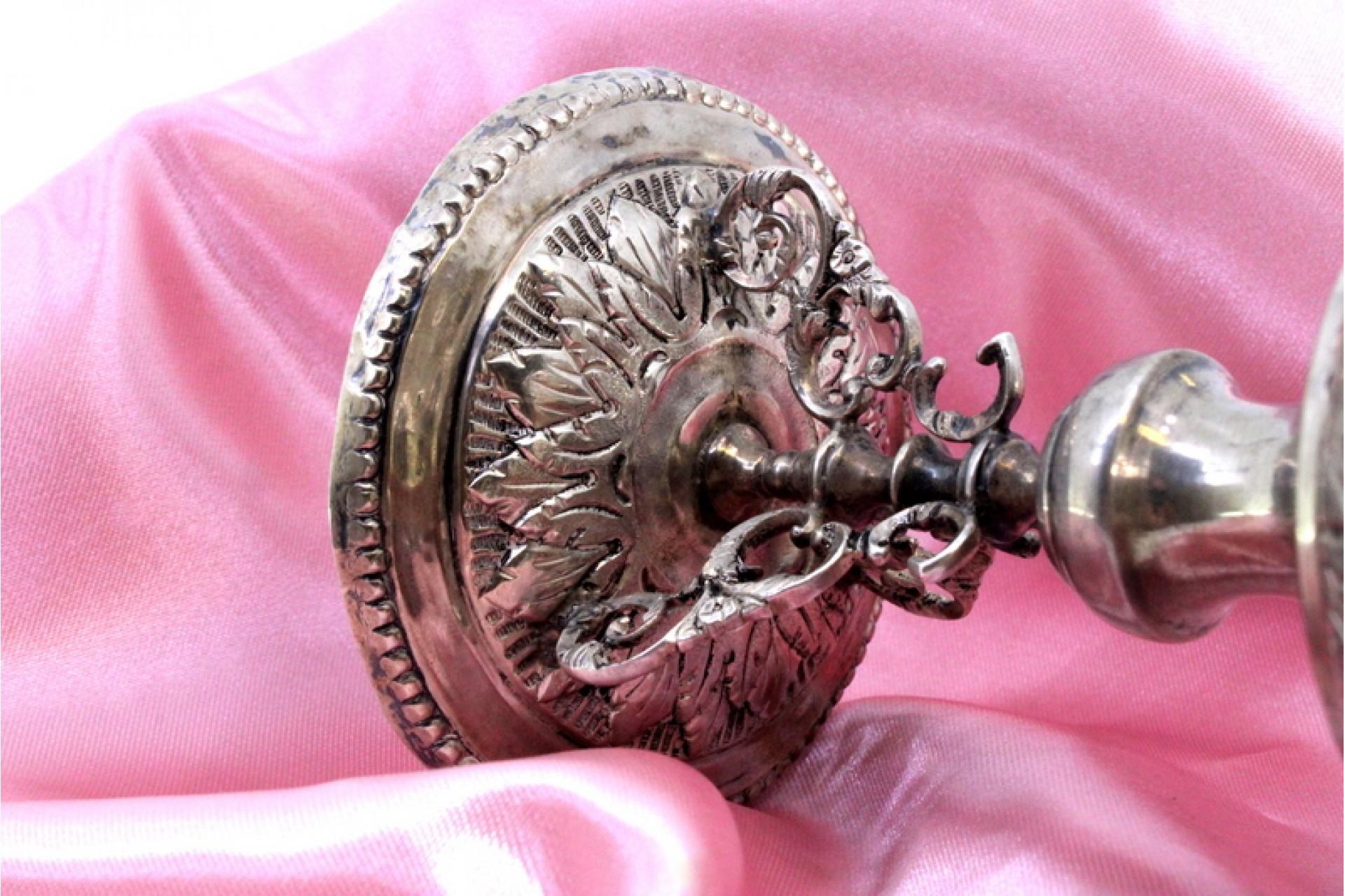 Description: Low silver candlestick with engravings and reliefs, resting on a round base with three feet with cut-out floral motifs. Metal: Silver. Origin: Portuguese. Brand: Javali II Title. Weight: 143.36 grams. Dimensions: 8cm x 13.5cm. Content: