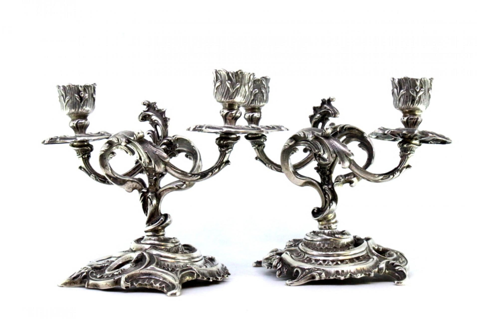Description: Low two-light silver candelabra with reliefs, shells, garlands, and applications set on cut-out bases. Metal: Silver. Origin: Portuguese. Brand: javali II Title. Weight: 1107.69 grams. Dimensions: 19cmx15cm. Content: 833/1000. Assay