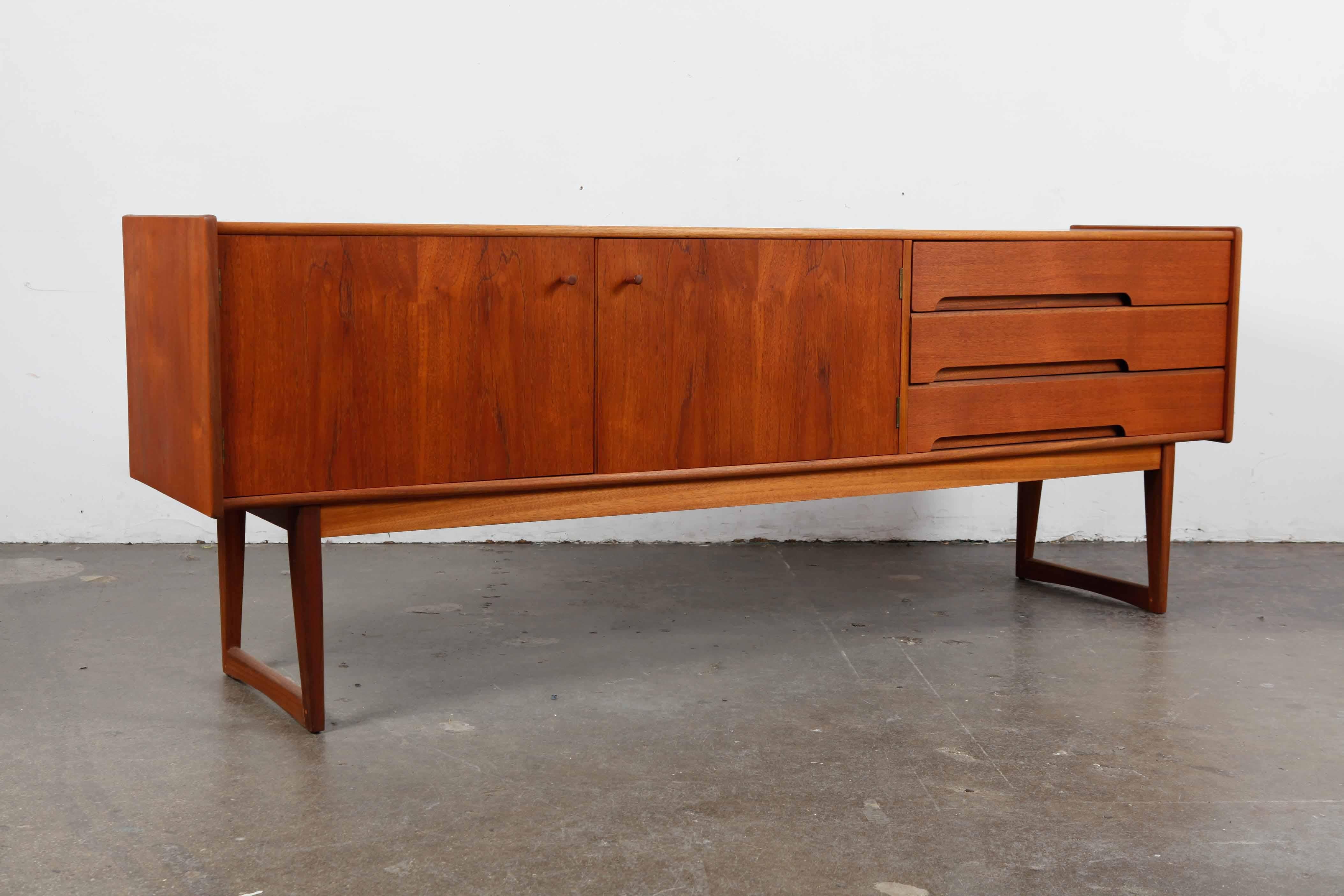 Teak low sideboard with very clean lines, 2 doors, 3 drawers with subtle inset drawer pulls and door handles, finished off with sleigh legs, produced by English maker A. Younger Ltd. Newly refinished in a natural matte teak oil finish.