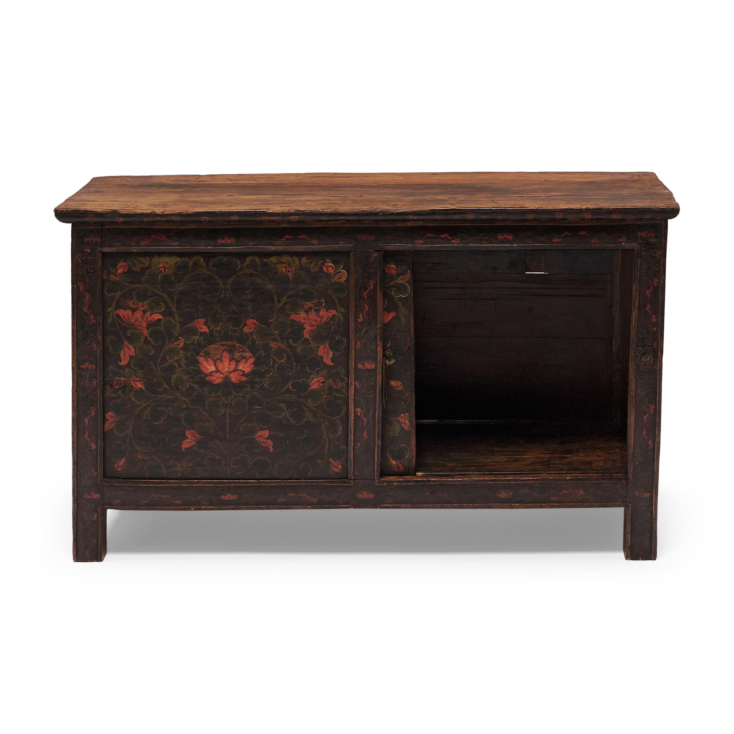 The front of this 19th-century Tibetan cabinet is beautifully painted with an allover pattern of flower blossoms and leaves. Brushed in a dark palette of green, gold and red-orange pigments, the floral design is simple yet effective, filling each