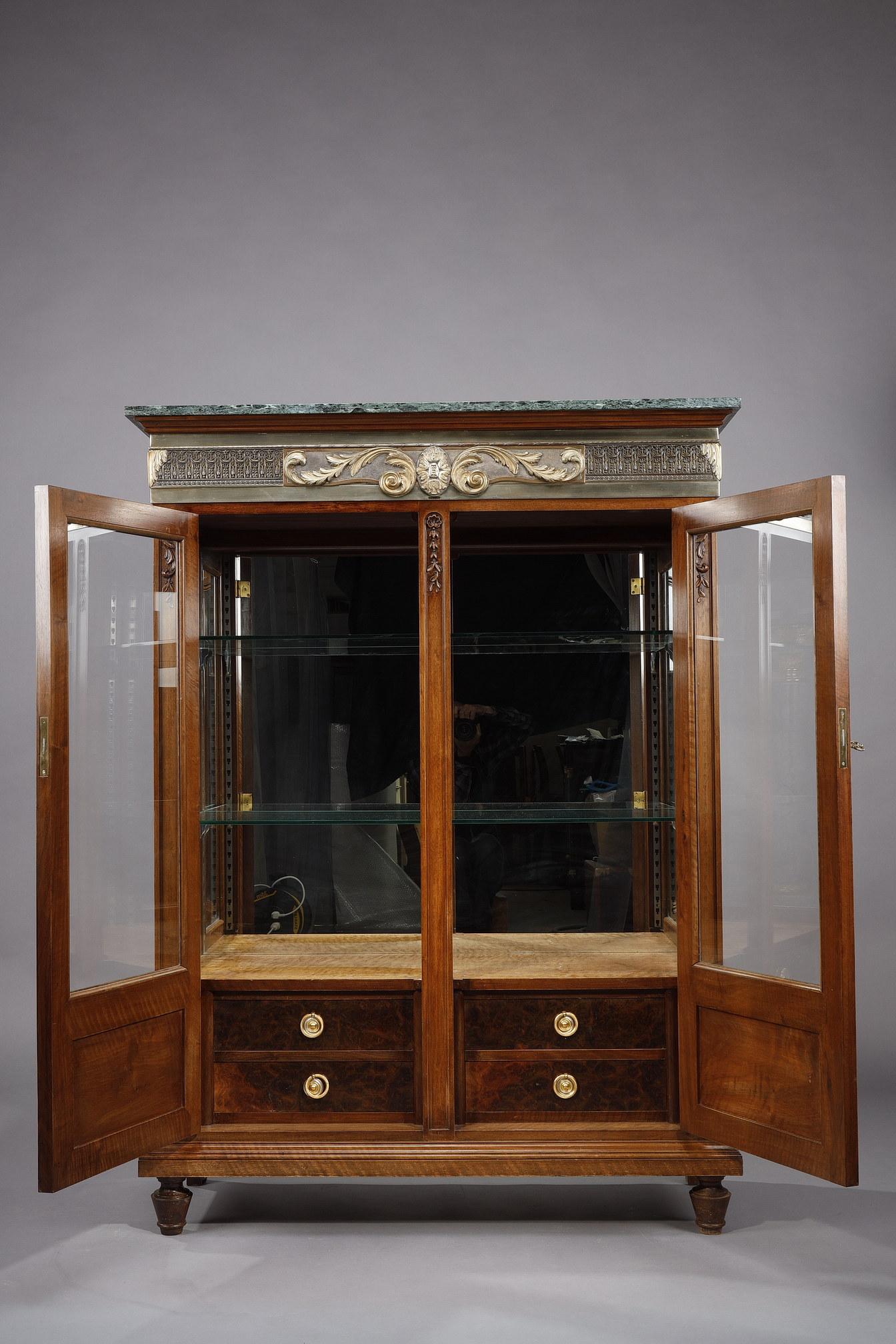 Low carved walnut display cabinet in the Louis XVI style opening with two doors on glass shelves and four drawers with double bottom including a cutlery set. The bookshelf is decorated with a large gilt bronze frieze with a front decorated with