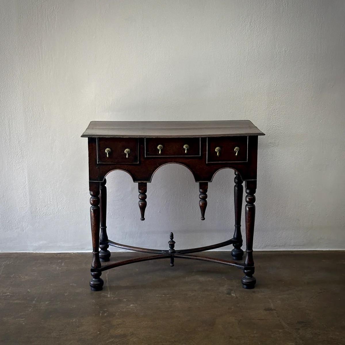 This exquisite 18th-century lowboy side table from England presents a masterful blend of form and utility. Its oak construction showcases deep, warm tones, enhanced by the original teardrop drawer pulls that add a touch of antique charm. The table