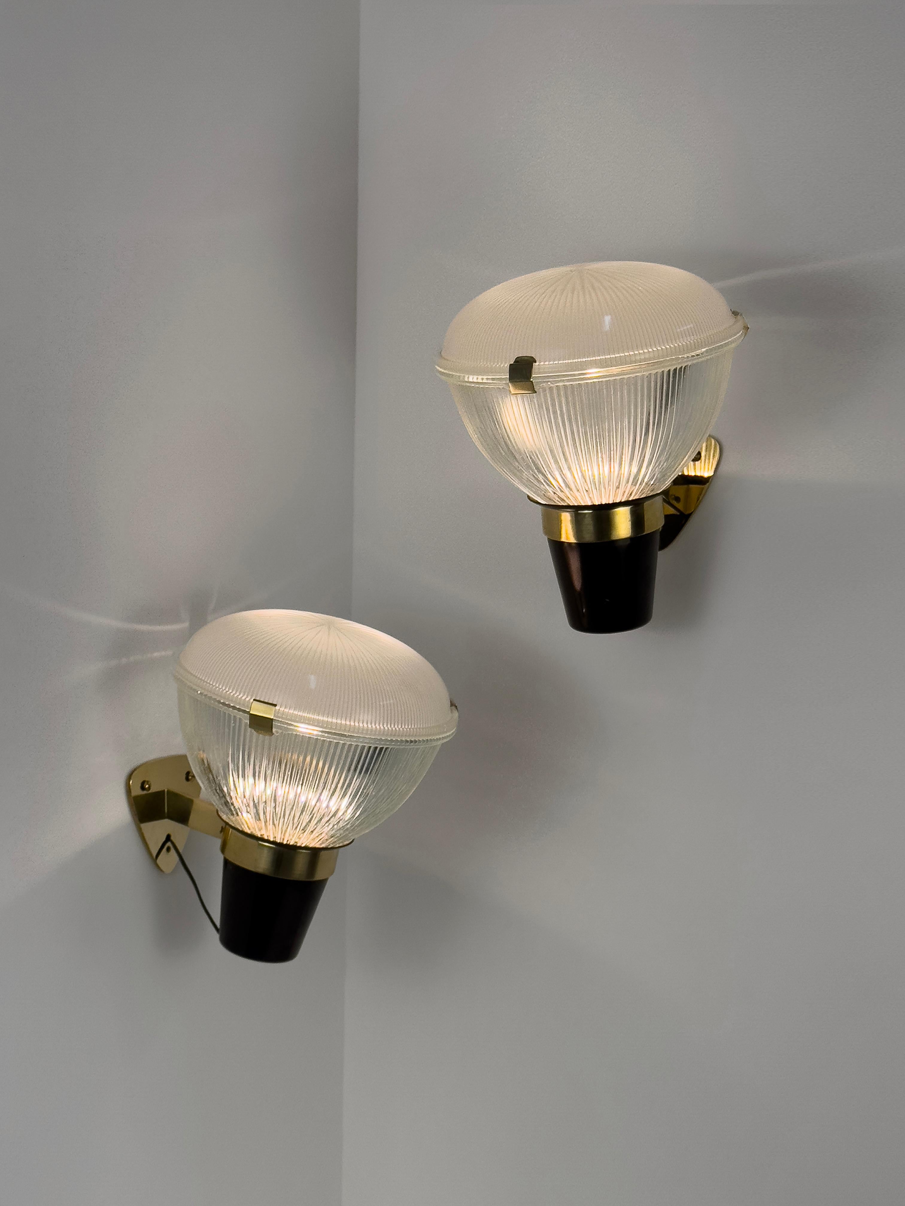Ces appliques emblématiques, conçues par Ignazio Gardella dans les années 1950 pour Azucena, présentent une combinaison frappante de métal peint en noir et de laiton, avec deux éléments en verre pressé ingénieusement maintenus ensemble par des