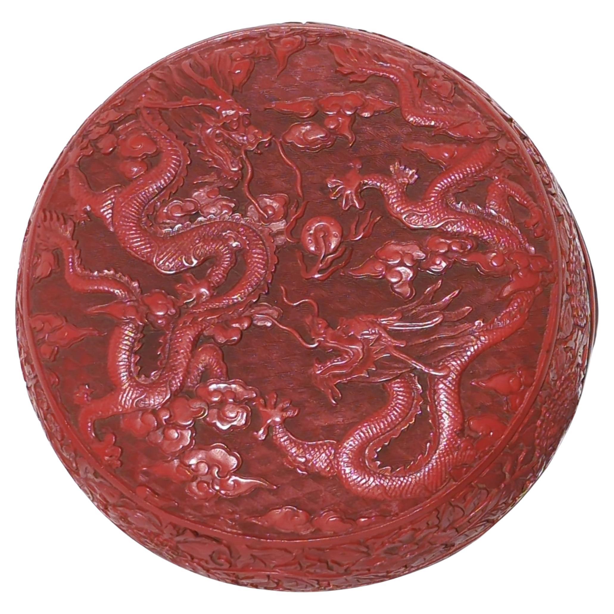 Large antique Chinese carved and painted cinnabar lacquer style covered round box, top decorated in relief with two fierce, scaly, slithering dragons chasing a flaming pearl amongst finely carved waves, with carved blossom and scrolling foliage to