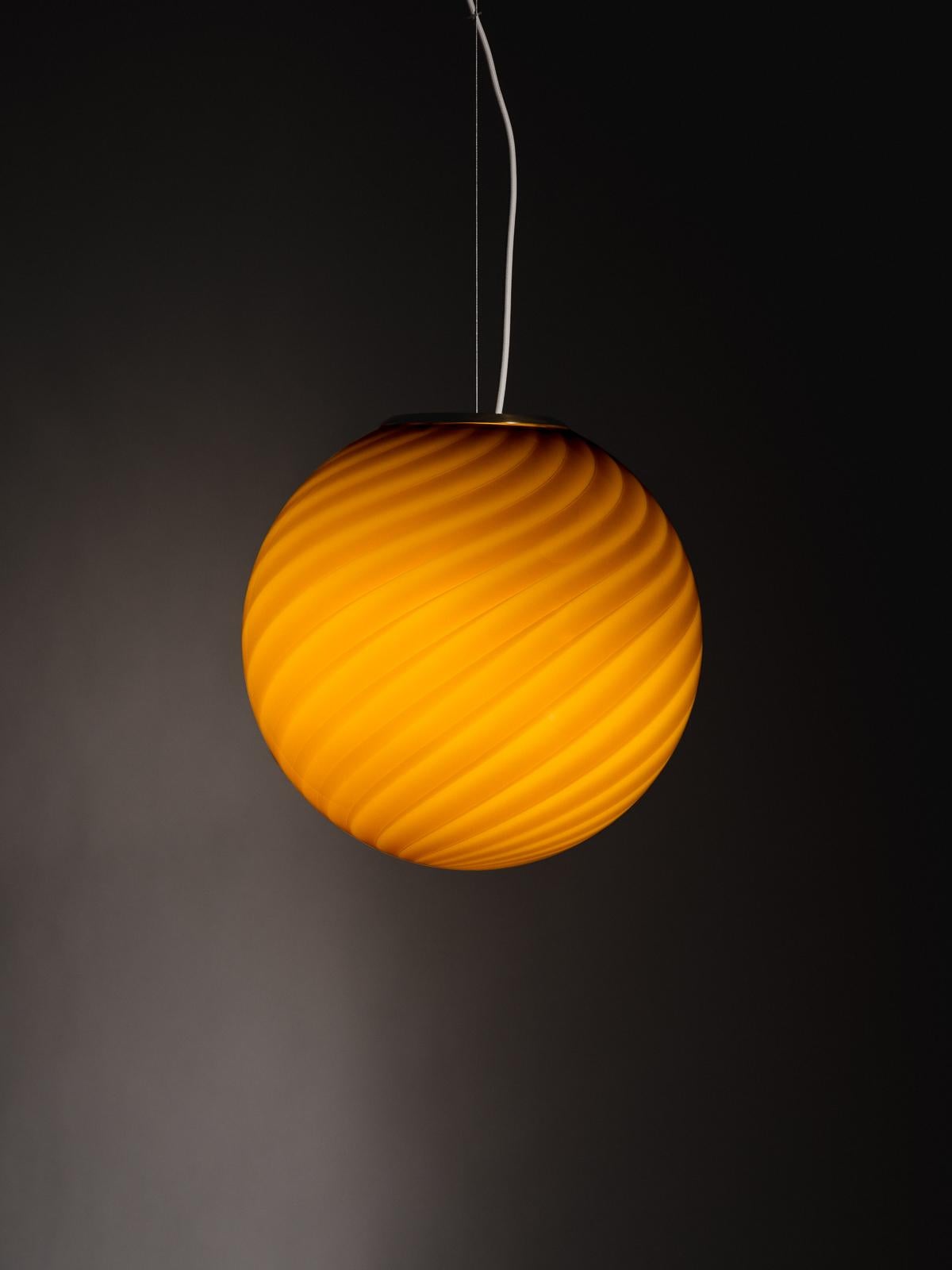 A limited edition of 50, this sculptural sphere-shaped pendant ceiling lamp is crafted from mouth-blown opaline glass in Ambra: a bright and warm hue with golden undertones. The lamp features an original swirl pattern obtained using a 1970s mould