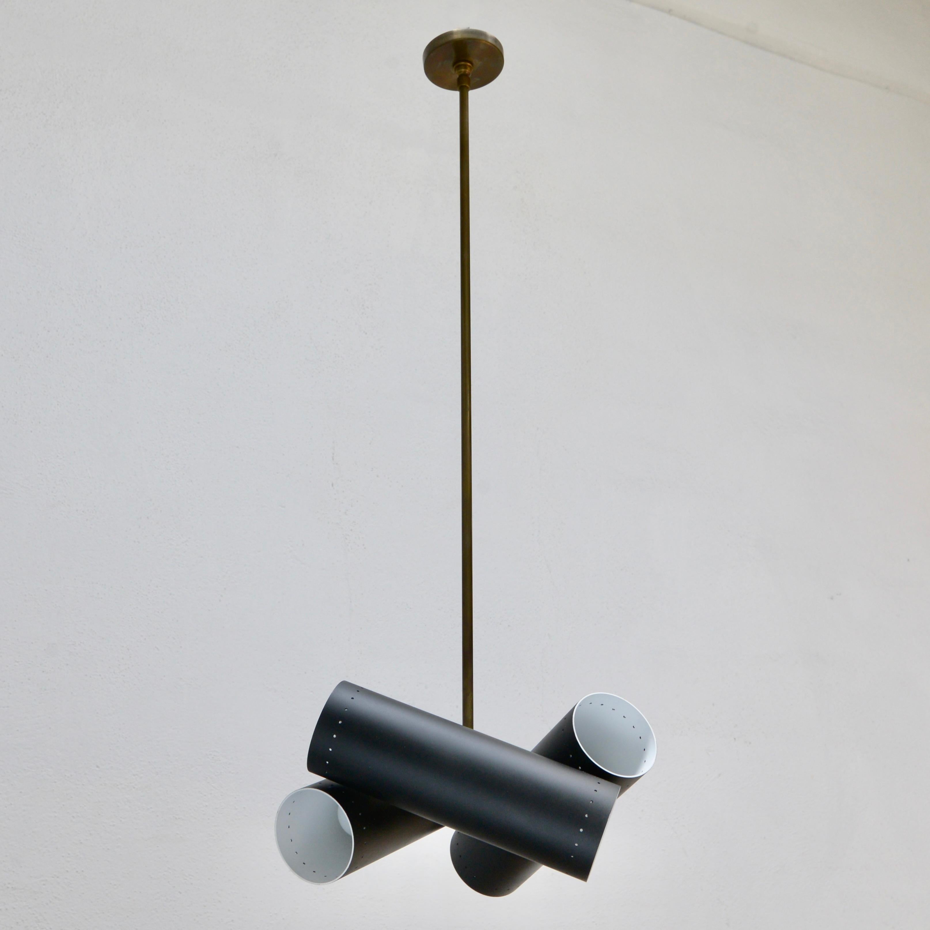 Modern, geometric LUbular Pendant SM is a smaller version of our LUbular Pendant. The fixture has three cylindrical tubular shades criss crossing to create directional light.  Made to order. Brass and painted aluminum finish. Custom finish and OAD